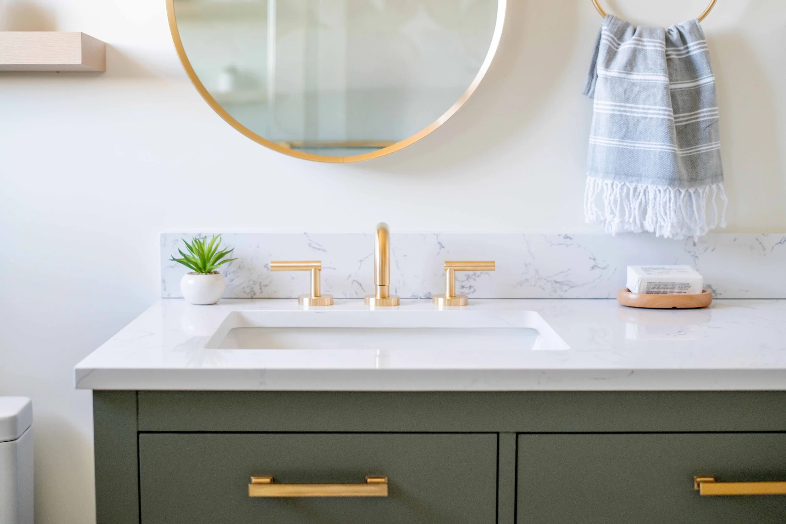 Bathroom renovation in a Tiburon home designed by Marin interior designer Studio SQUIRE featuring a sage green vanity, brass plumbing fixtures, and quartz countertops.