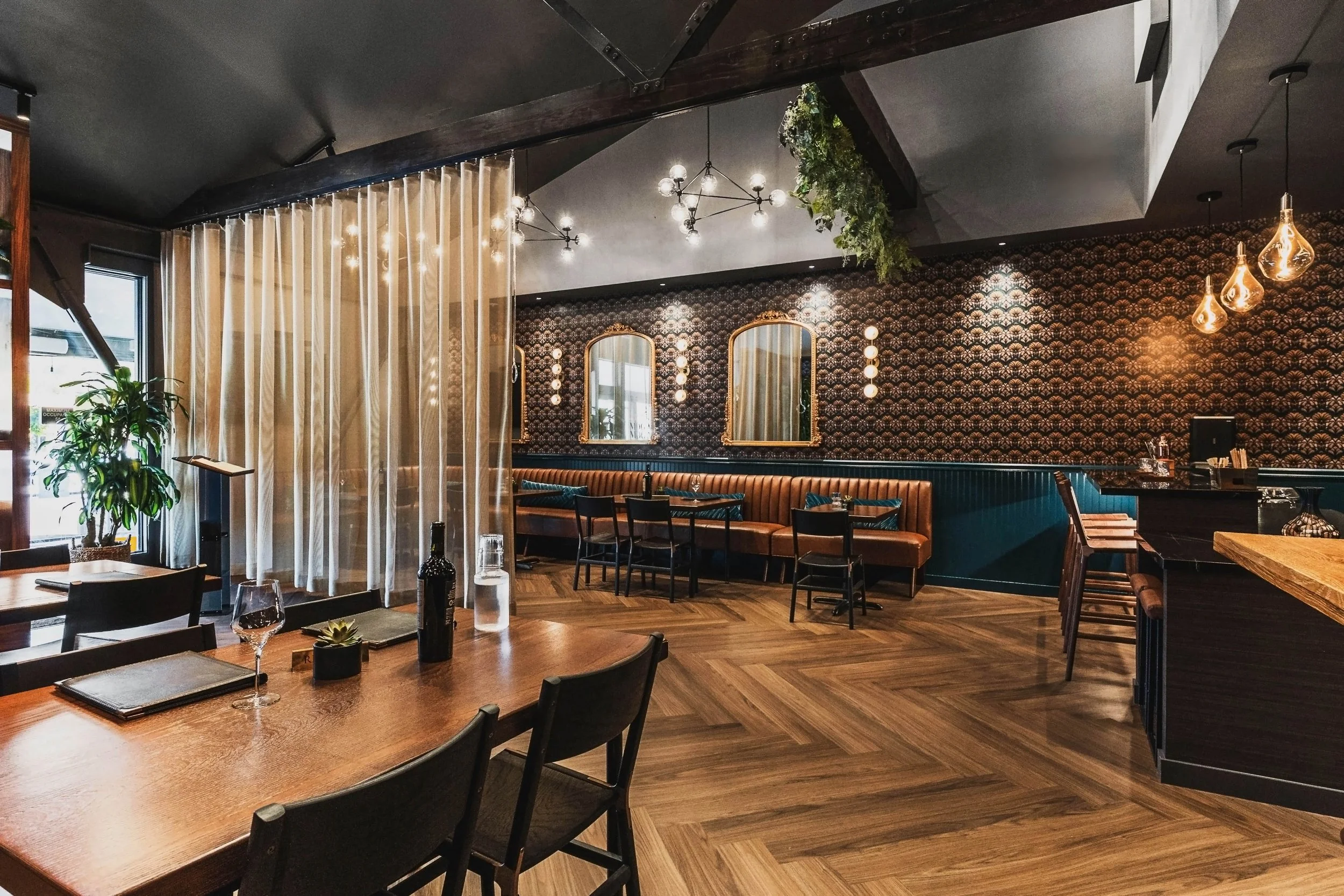 Commercial wine bar renovation in Belvedere-Tiburon designed by Marin interior designer Studio SQUIRE featuring Herringbone Wood Flooring, Banquette Seating, Patterned Wallpaper, Brass Mirrors, and Wall Paneling