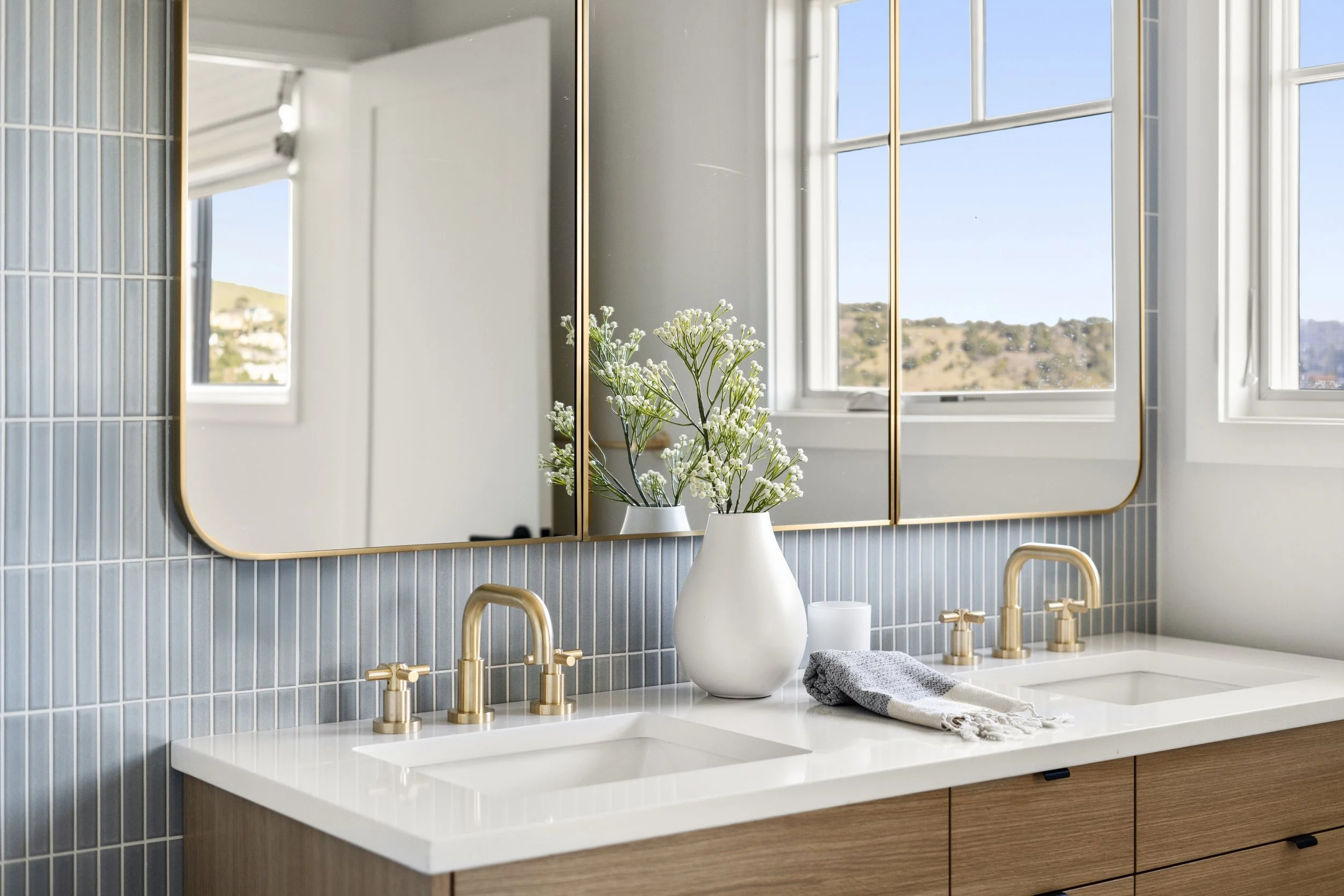Primary bathroom renovation in a Tiburon home designed by Marin interior designer Studio SQUIRE featuring a white oak vanity, blue tile, brass plumbing fixtures, and quartz countertops.