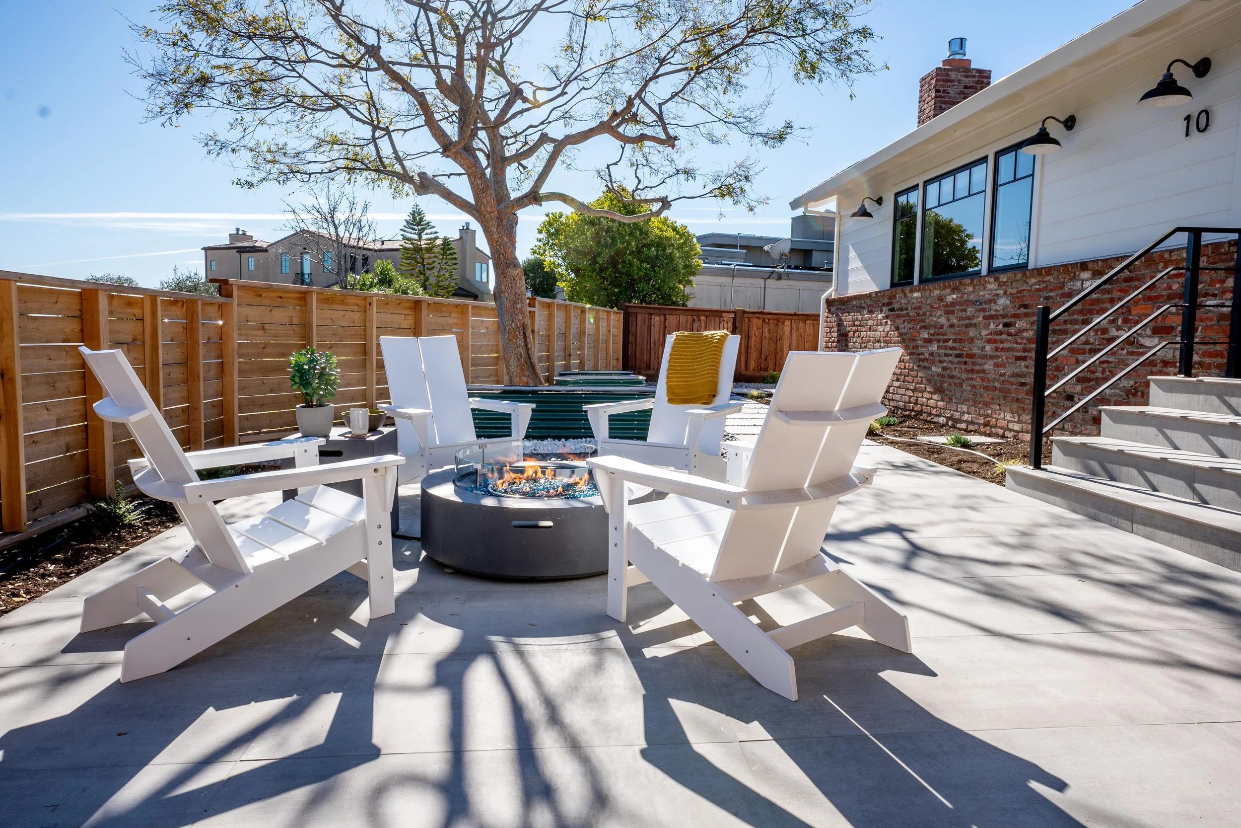 Outdoor living space designed by Marin interior designer Studio SQUIRE for a Tiburon home featuring white adirondack chairs, a modern round fire pit, and a porcelain paver patio.