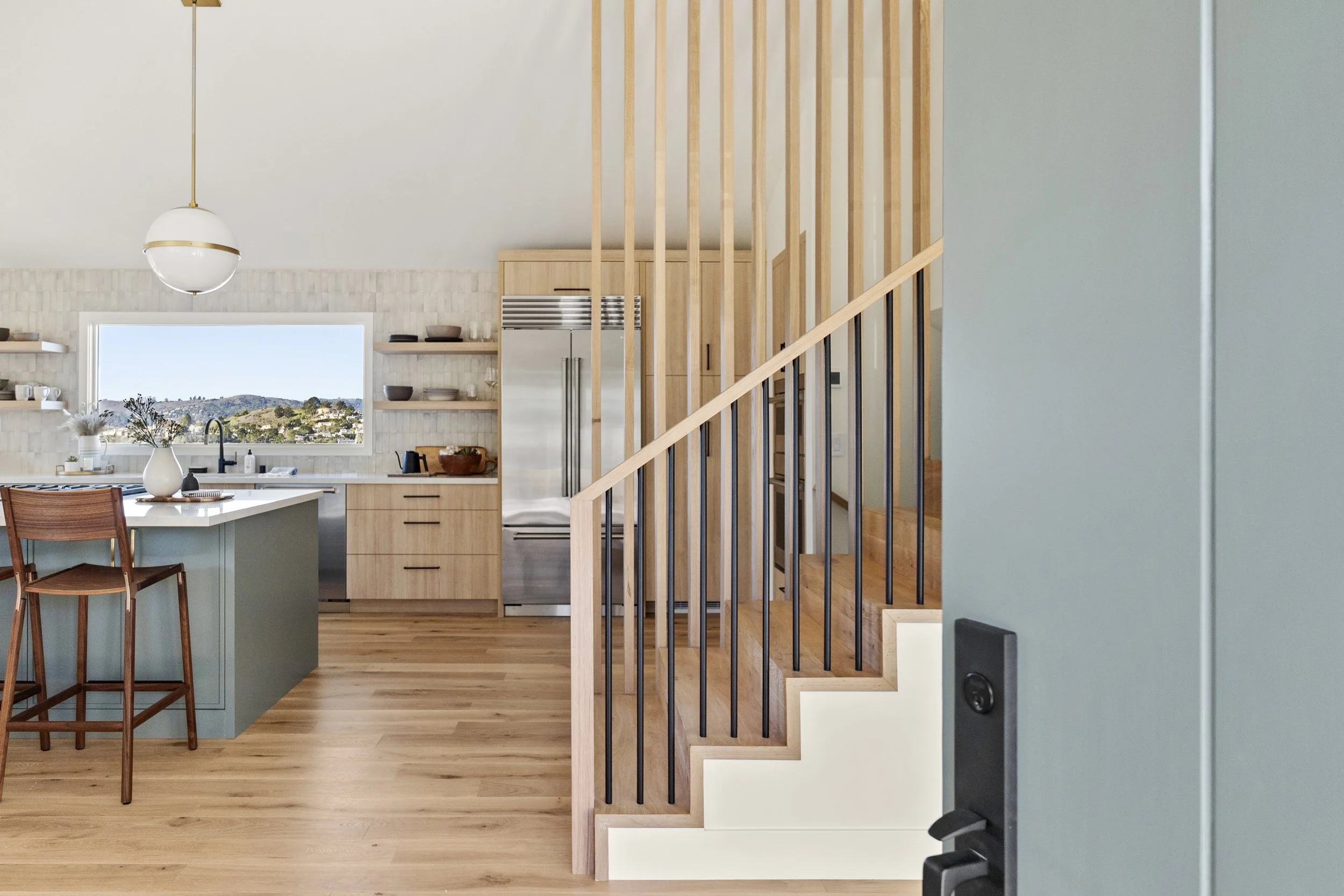 Kitchen renovation in Tiburon designed by Marin interior designer Studio SQUIRE featuring white oak custom cabinets, open shelving, a sage green island, and views.
