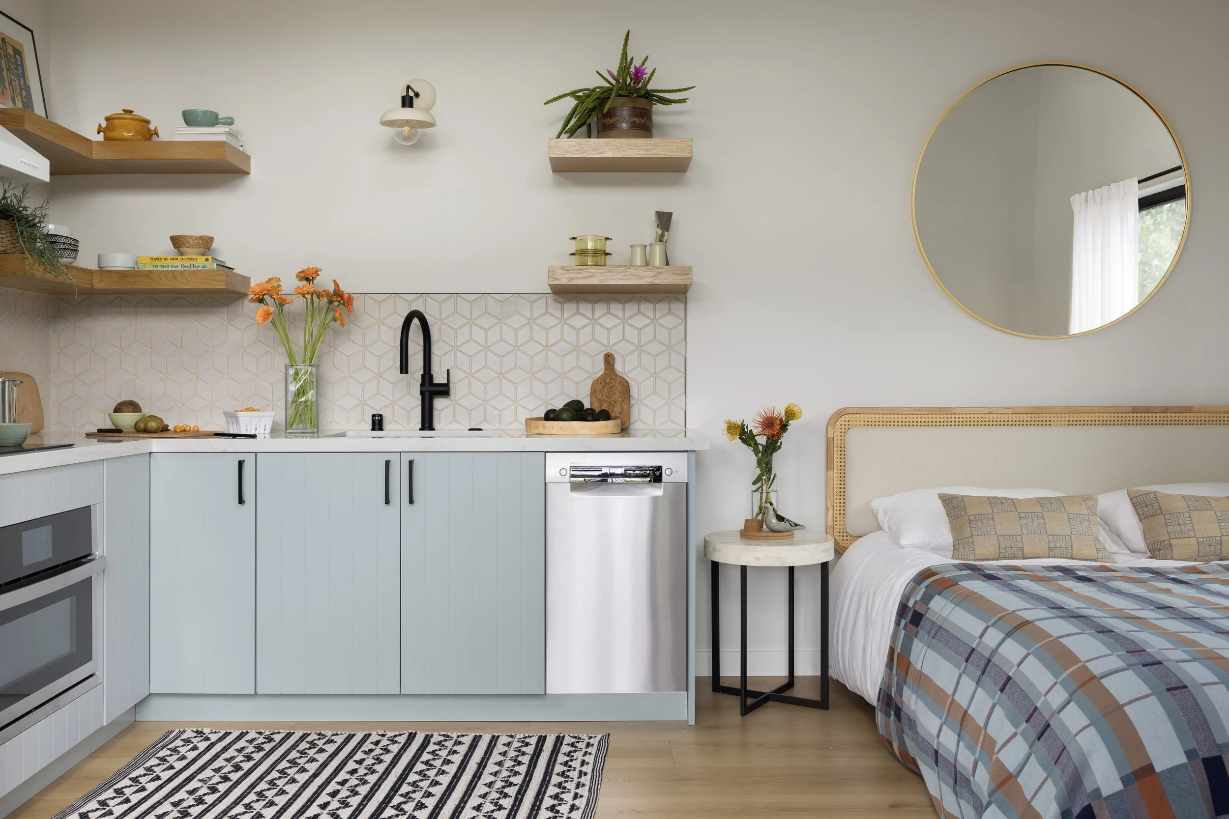 ADU renovation in Mill Valley designed by Marin interior designer Studio SQUIRE featuring quartz countertops, matte black hardware, wood shelves, gold round mirror, and rattan bed