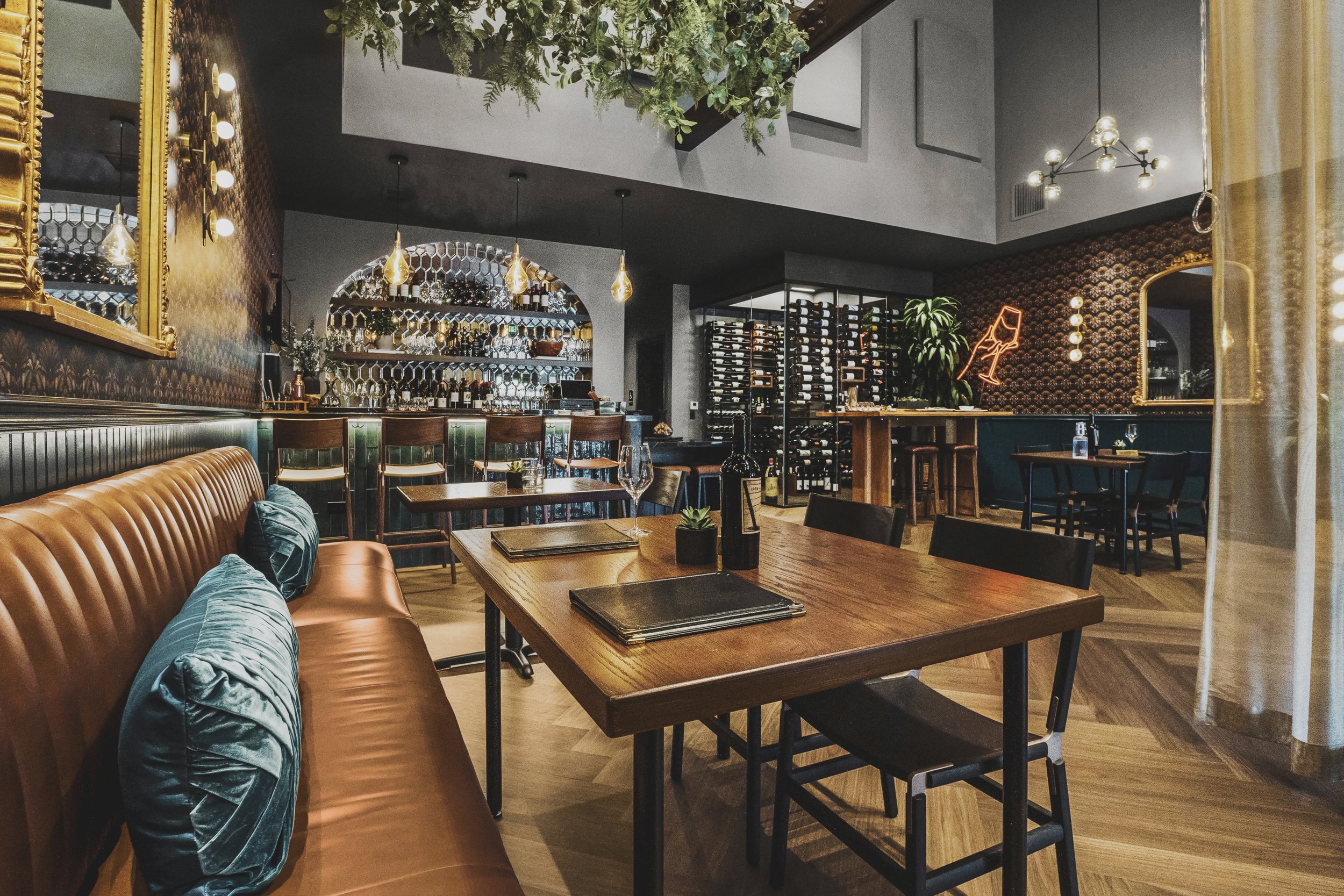 Wine bar renovation in Belvedere-Tiburon designed by Marin interior designer Studio SQUIRE featuring walnut floors, leather, banquettes, art deco inspired decor, modern lighting fixtures, and lush plants throughout.