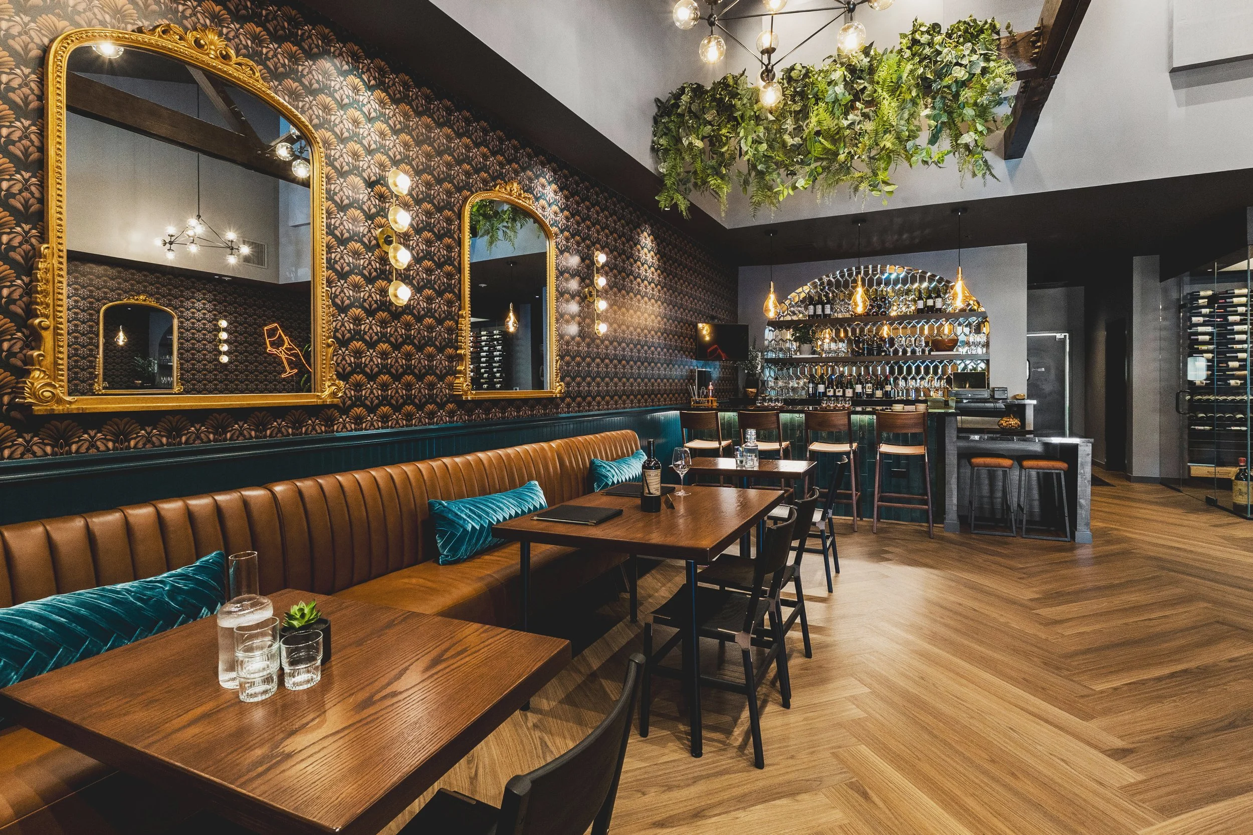 Commercial wine bar renovation in Belvedere-Tiburon designed by Marin interior designer Studio SQUIRE featuring Banquette Seating, Brass Mirrors, Herringbone Wood Flooring, Patterned Wallpaper, Wood Tables, and Black Side Chairs