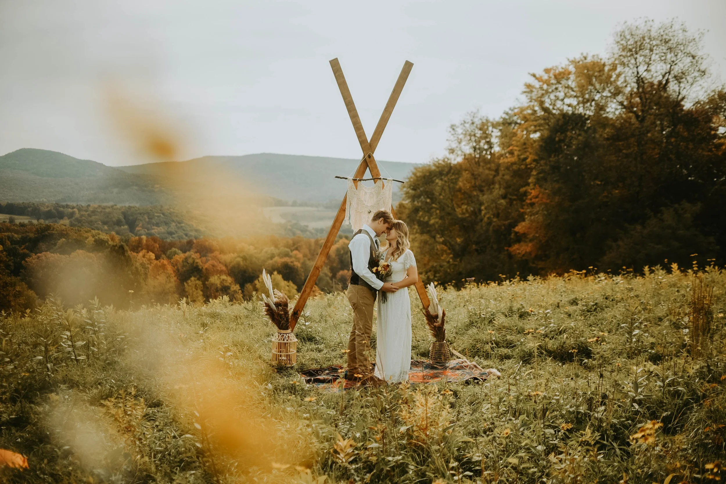 couple standing in field holding hands and looking into eachothers eyes with wedding arch and rolling hills behind them.jpg