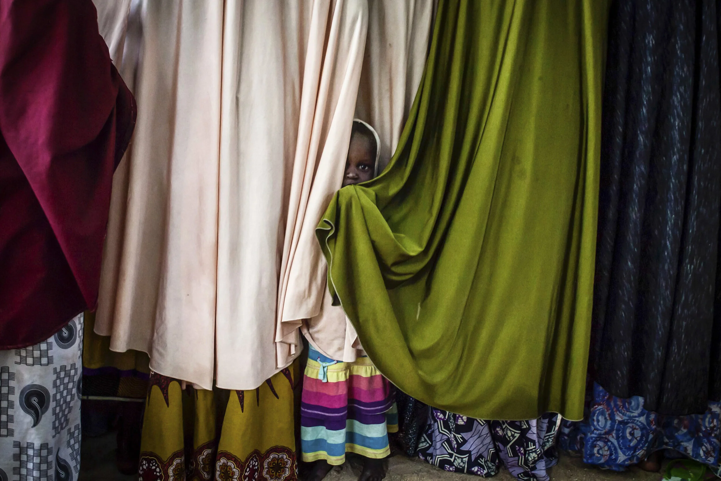 The daughter of a former Boko Haram commander plays between the chadors of their wives at a "safe house" in Maiduguri, Nigeria.