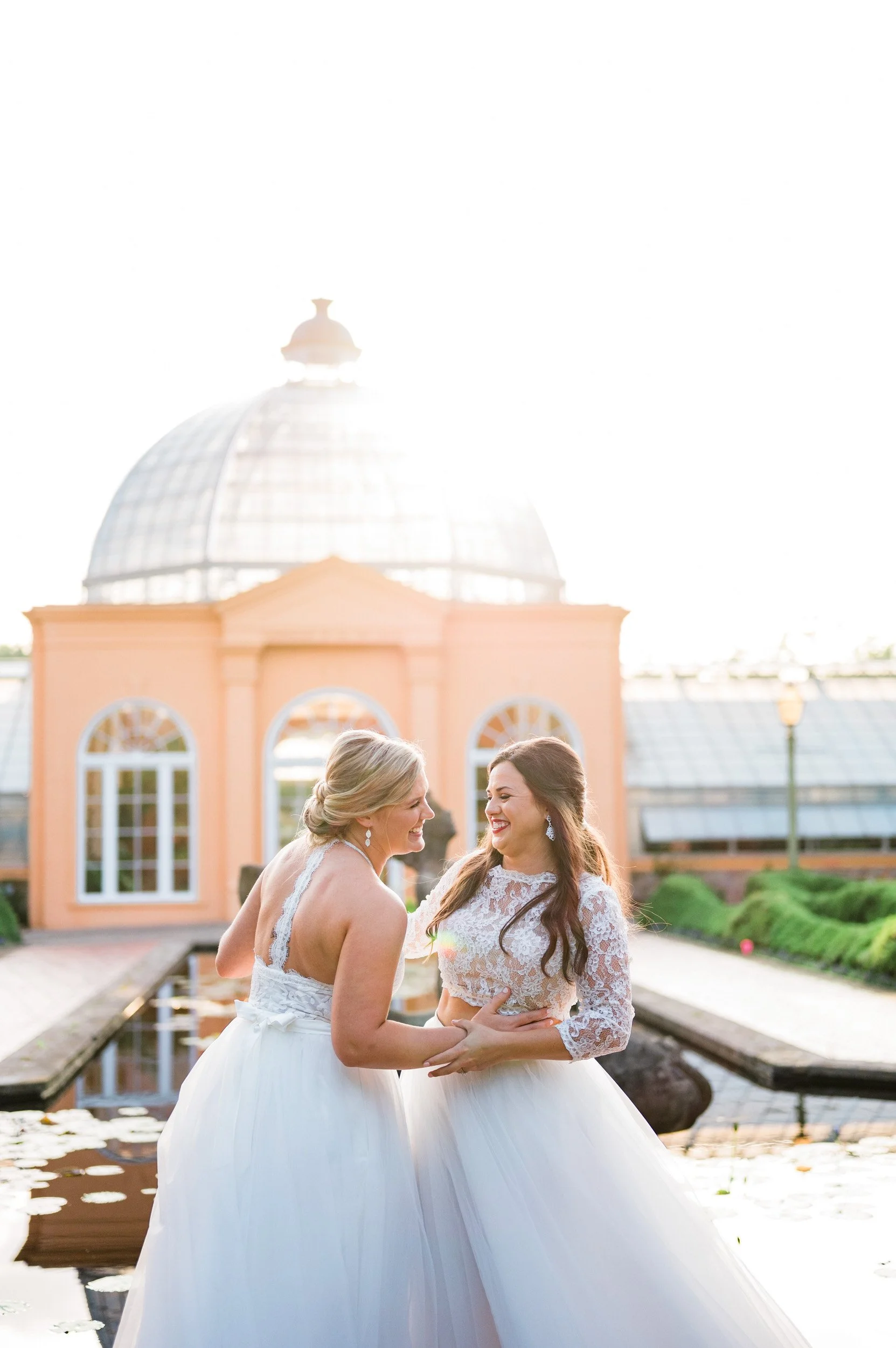 Newlyweds laughing with their arms around each other while standing in front of a pond