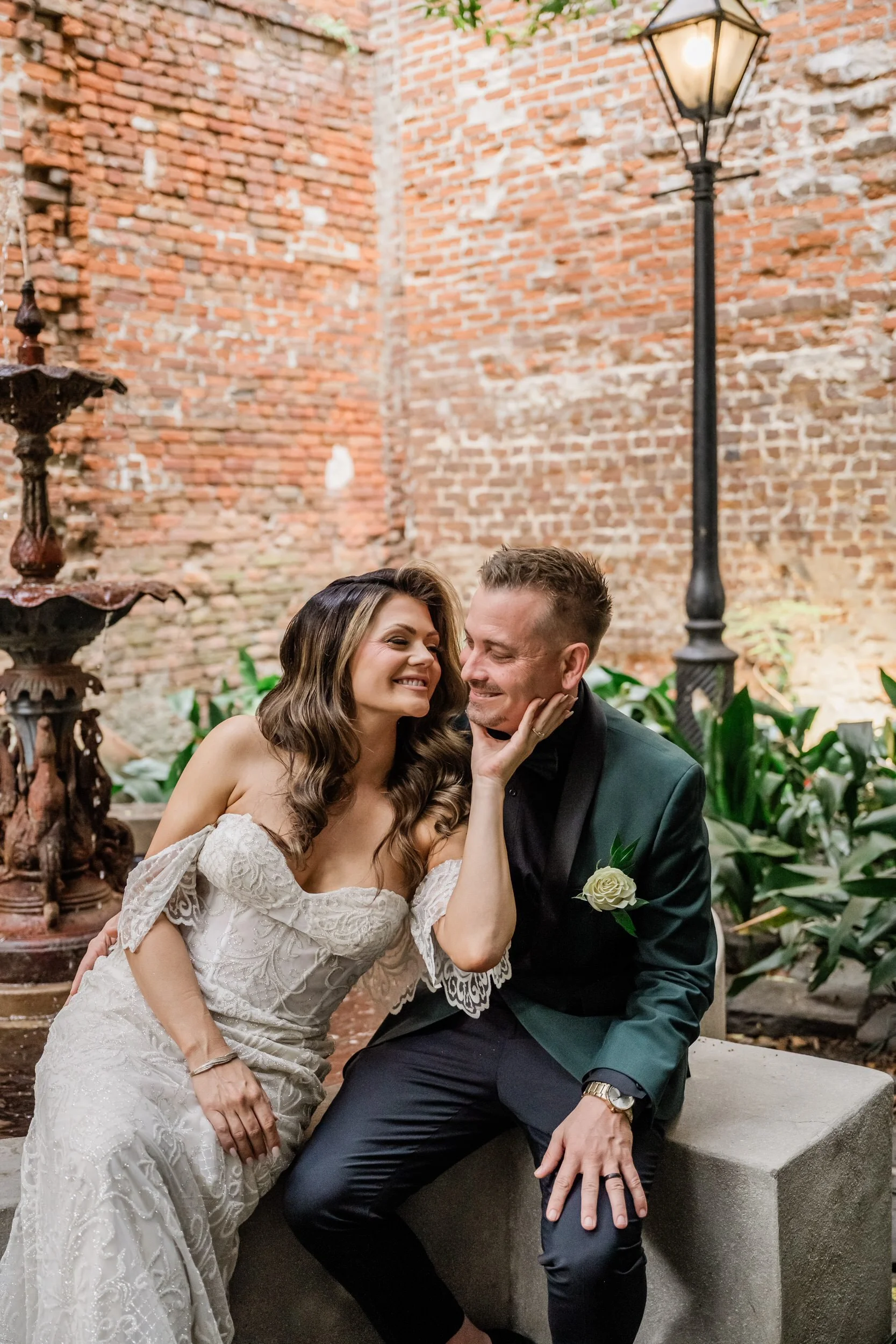 A newlywed couple sitting together while one leans into the other and holds their chin
