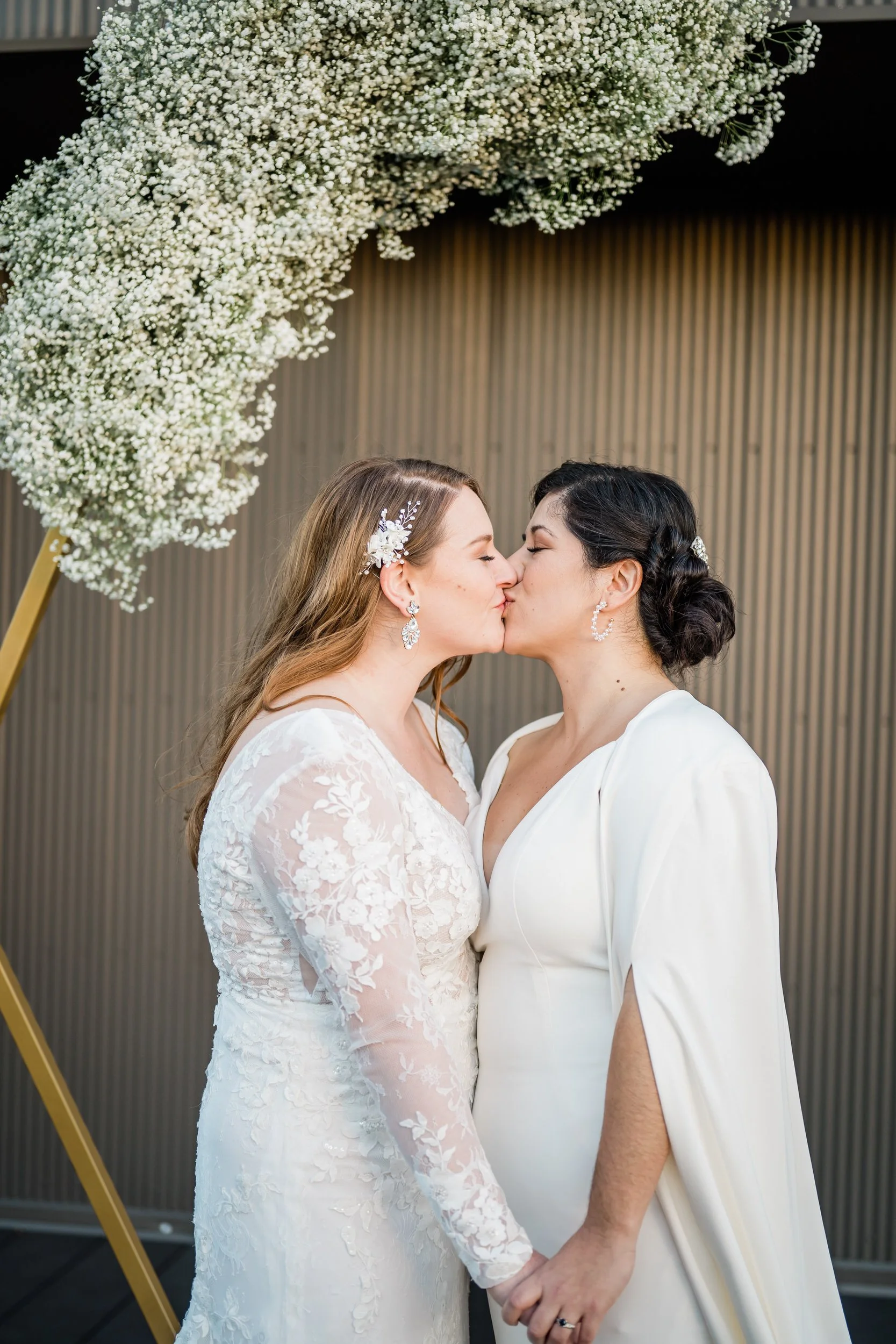 A newlywed couple holding hands as they kiss