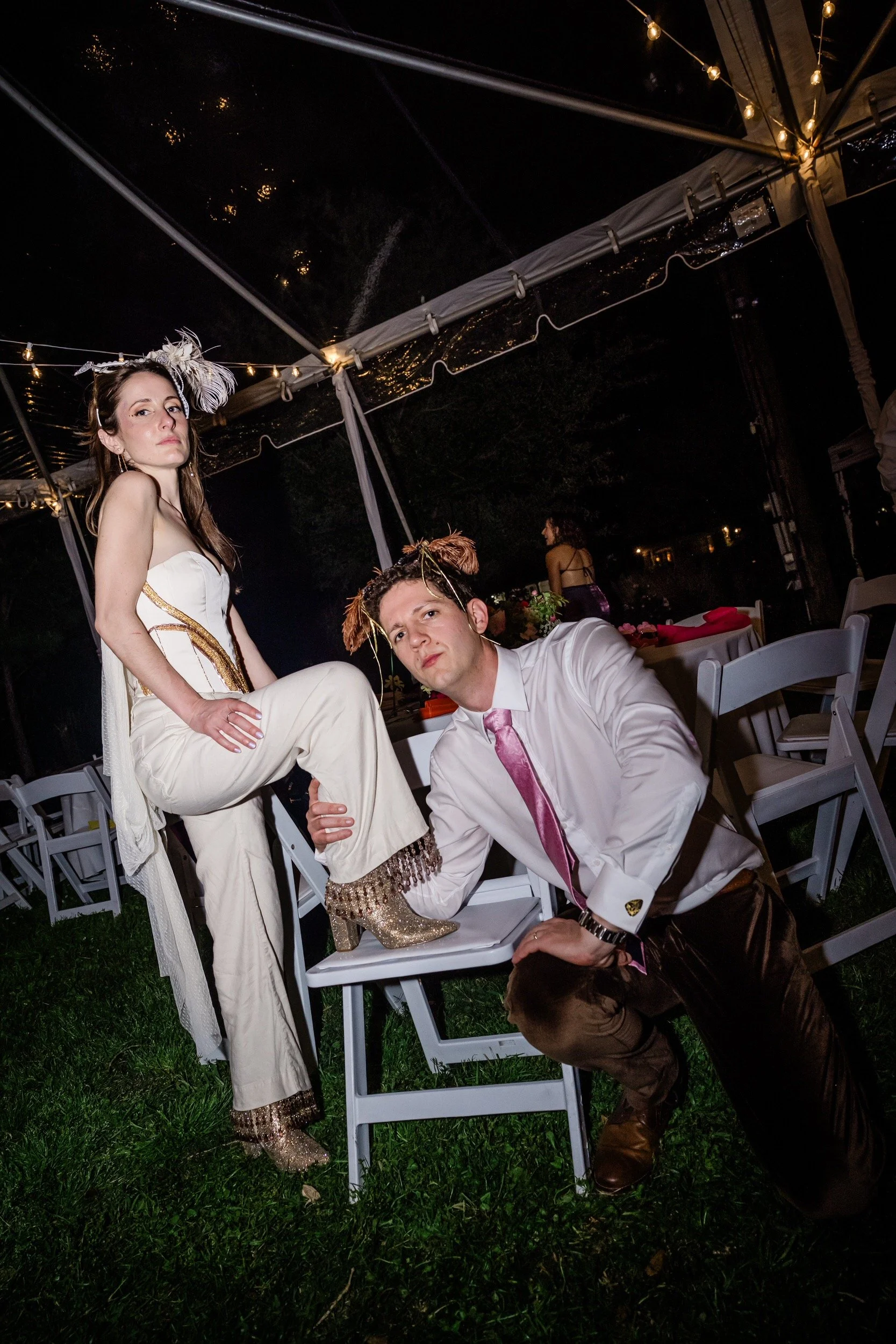 A newlywed kneeling on the ground grabbing the ankle of their partner that is lifted on top of a chair