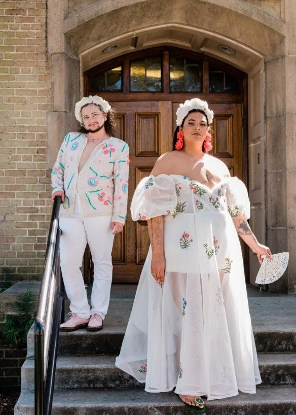 A newlywed couple standing one in front of the other on a small staircase after their wedding