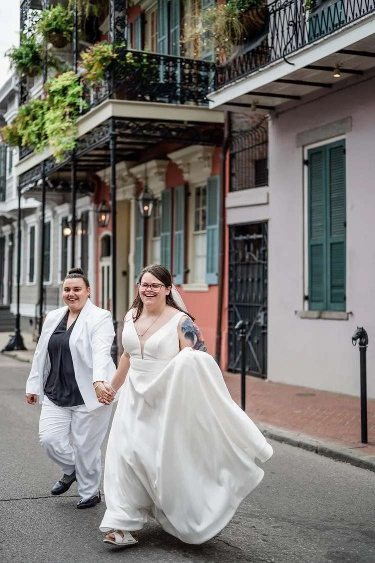 Newlyweds holding hands and laughing as they walk across a street
