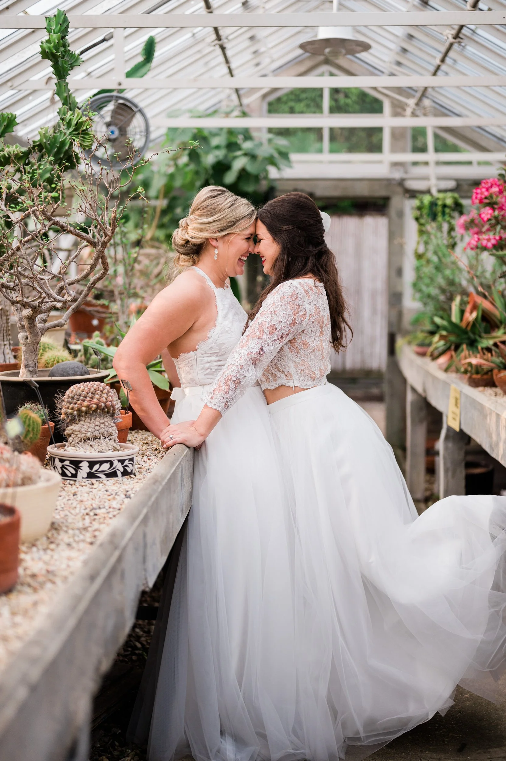 Newlyweds standing in a greenhouse as they are forehead to forehead smiling at each other 