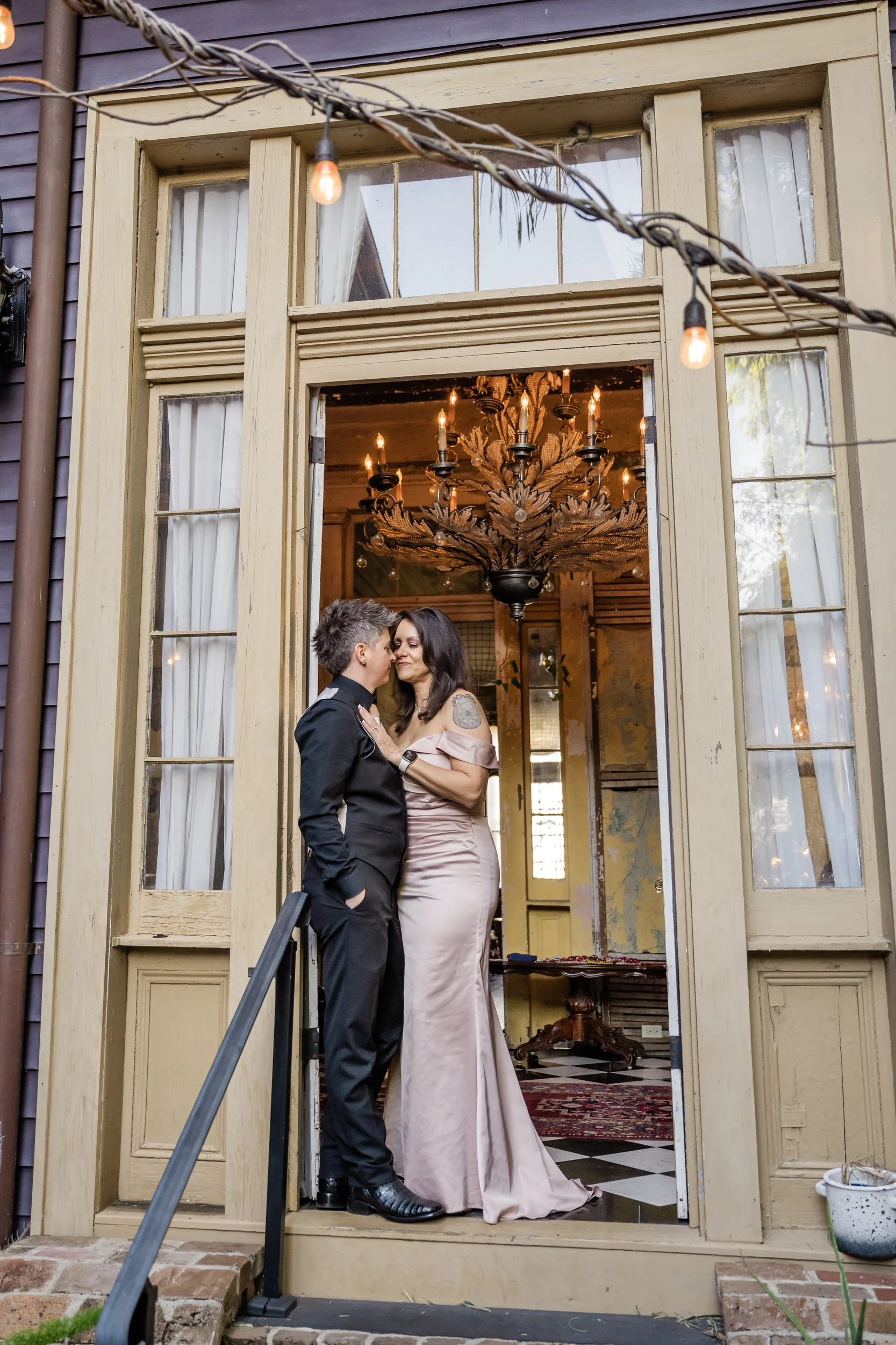 A newlywed couple standing close together with their arms around each other in the frame of a door