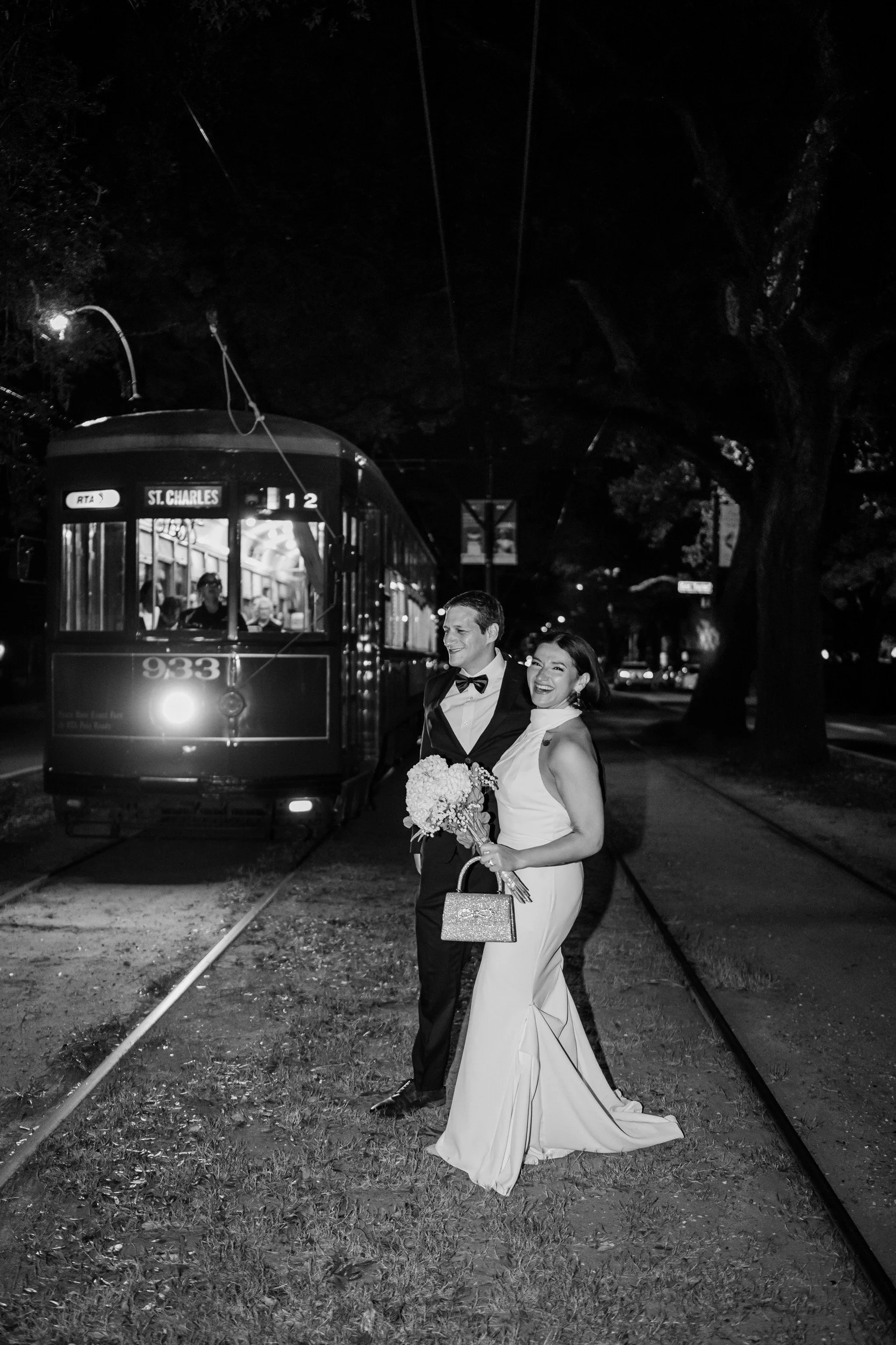 A newlywed couple laughing as they walk across a street in front of a cable car