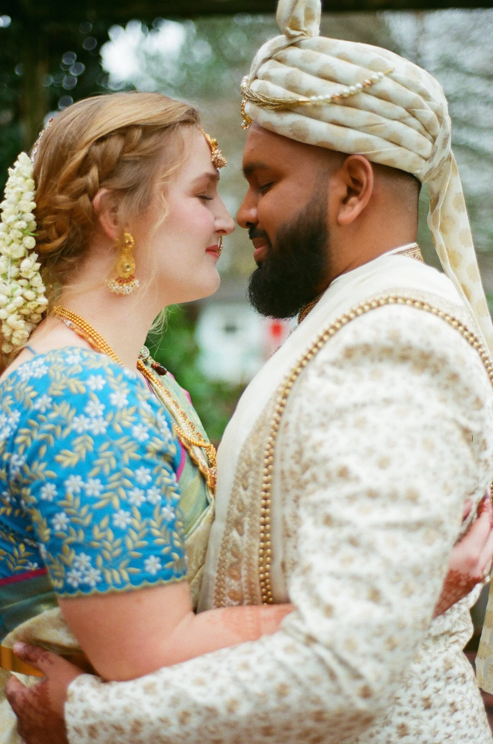 A couple in traditional wedding outfits standing nose to nose as they smile 