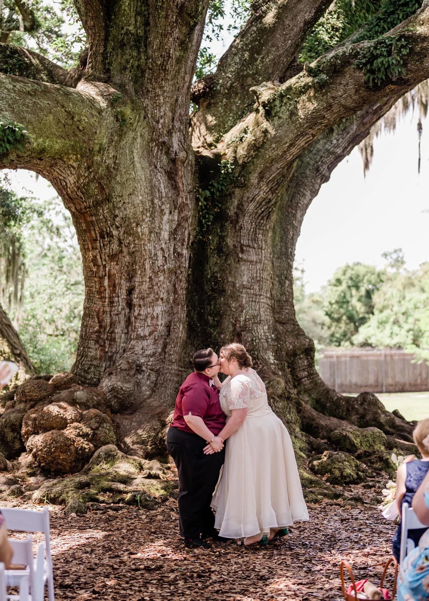 Newlyweds during their first kiss in front of a large tree