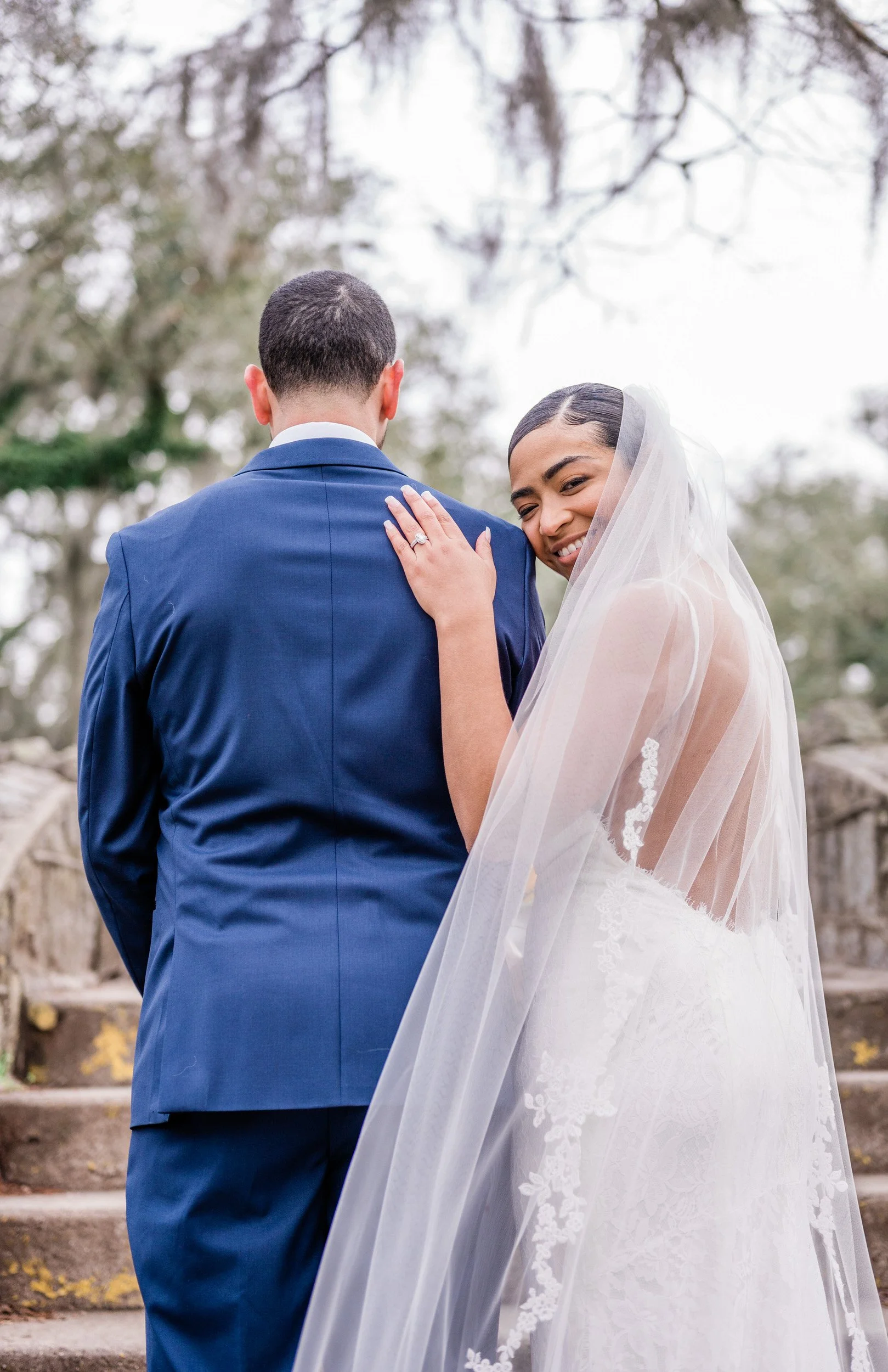 Newlyweds standing side by side as one looks back over their shoulder and smiles