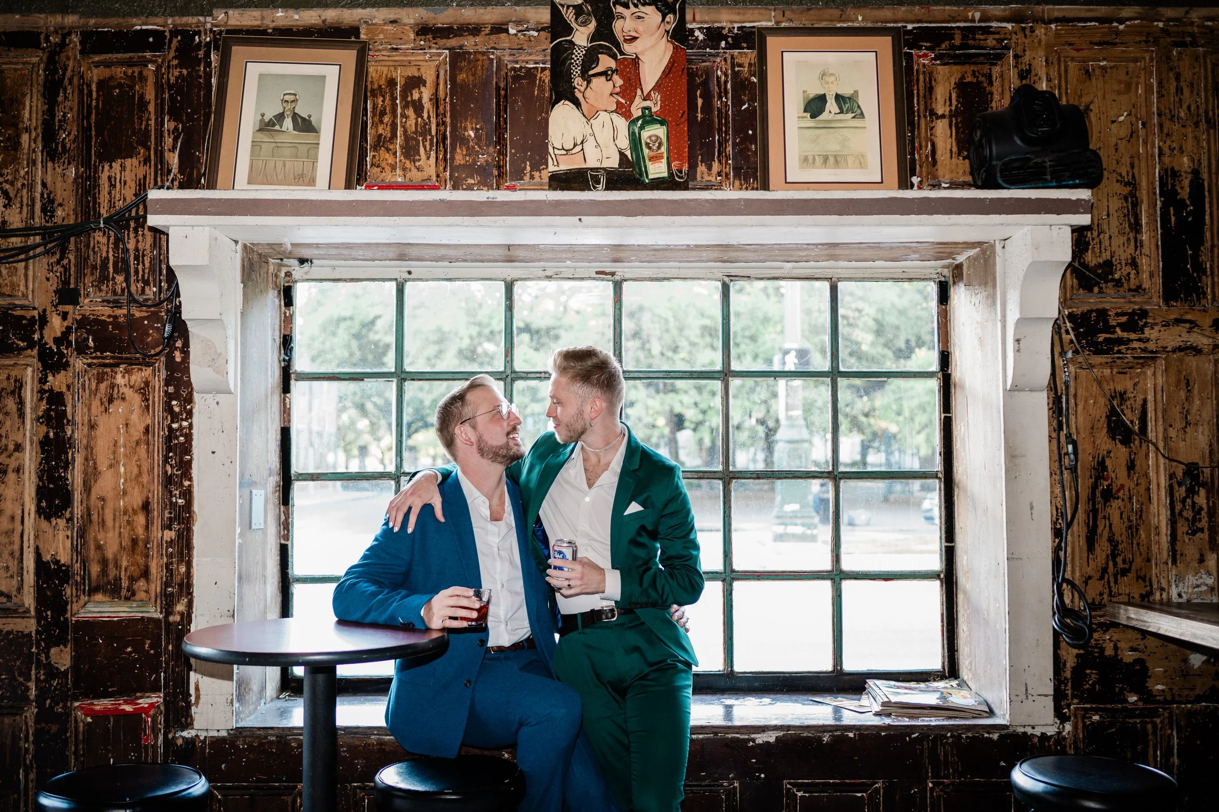 A couple with their arms around each other as they look at each other and smile while both holding drinks