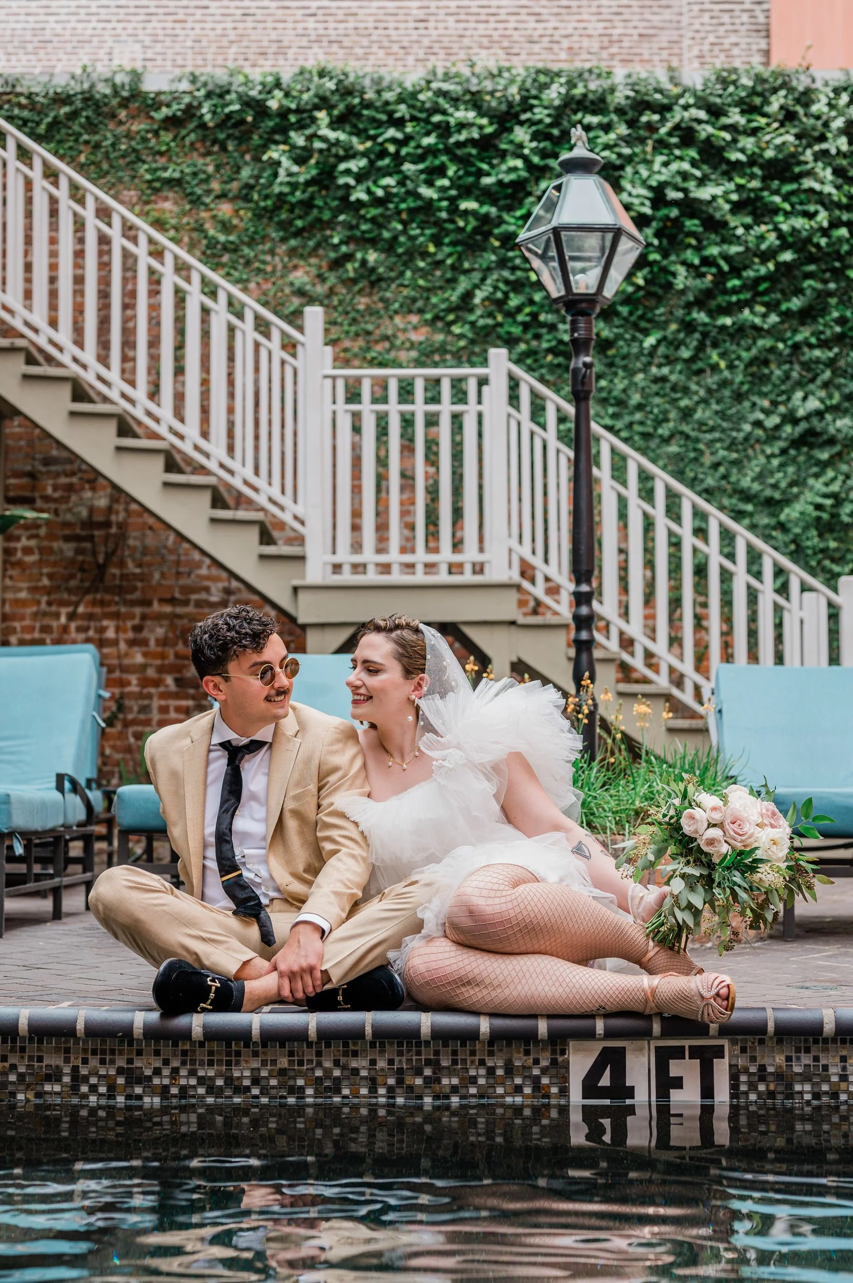 A newlywed couple sitting close and leaning into each other along the edge of a pool