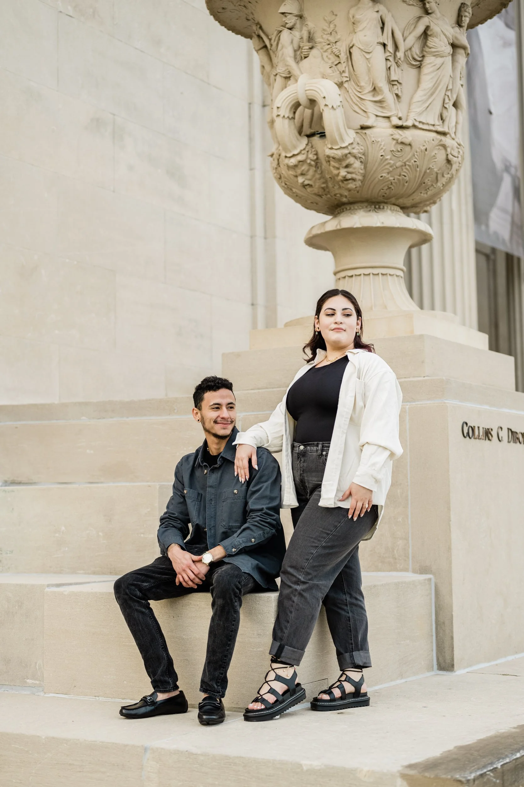 A person sitting on a stone staircase with their partner standing next to them resting their arm on their shoulder