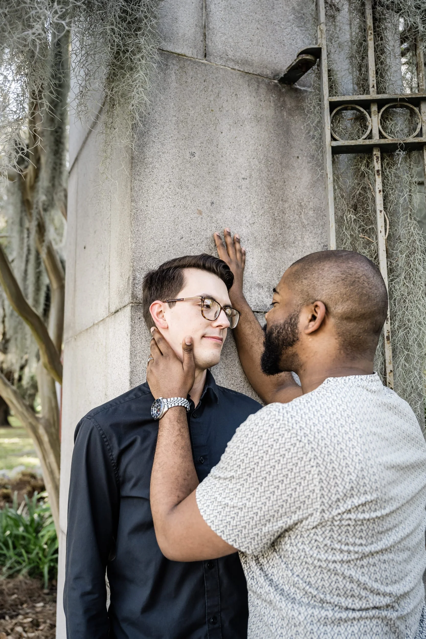 A couple standing against a pillar as one has their hand on the other's cheek