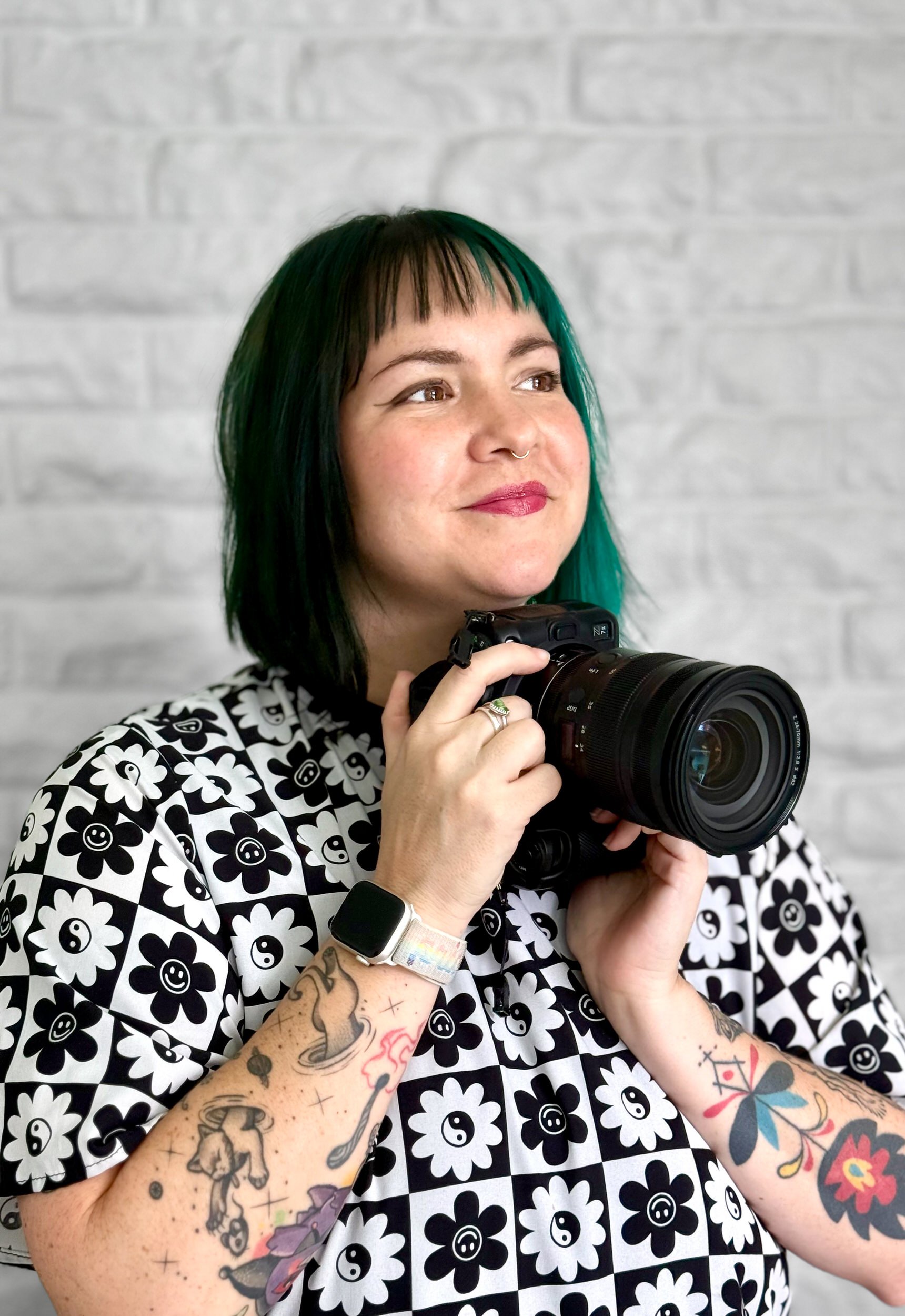 Ash smiling and looking off to the side as she holds a camera