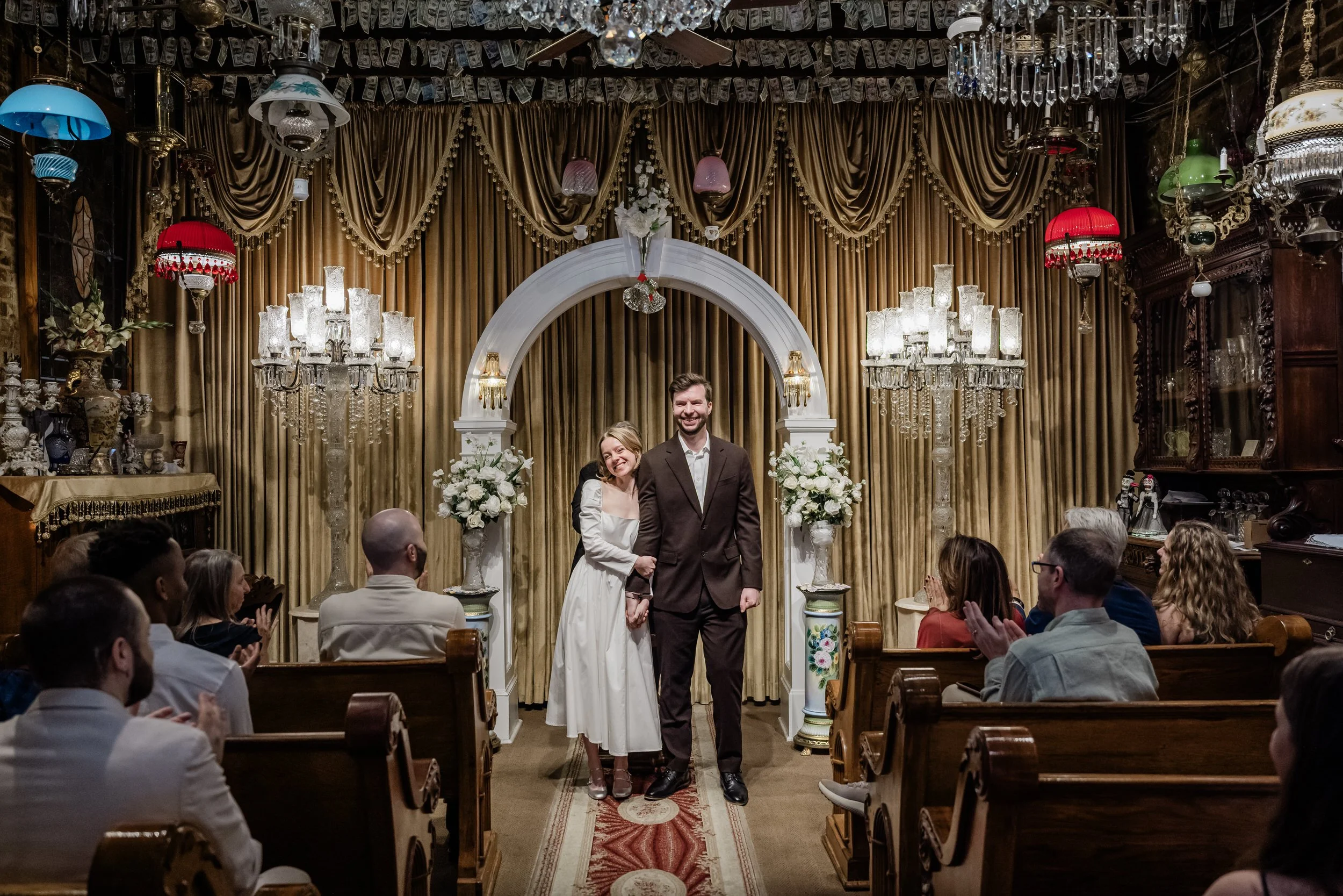 A newlywed couple smiling as they hold hands and walk back up the aisle