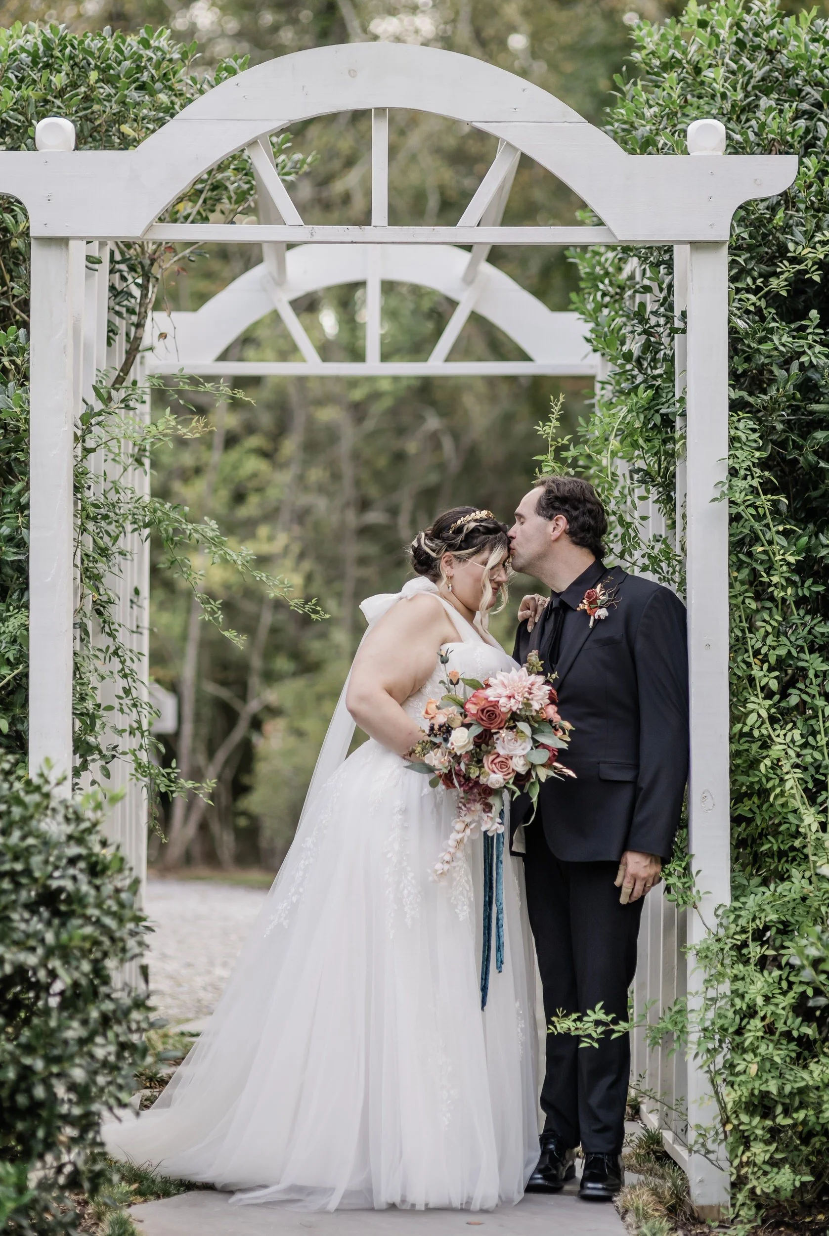 A newlywed kissing their partner's forehead as they stand in a garden