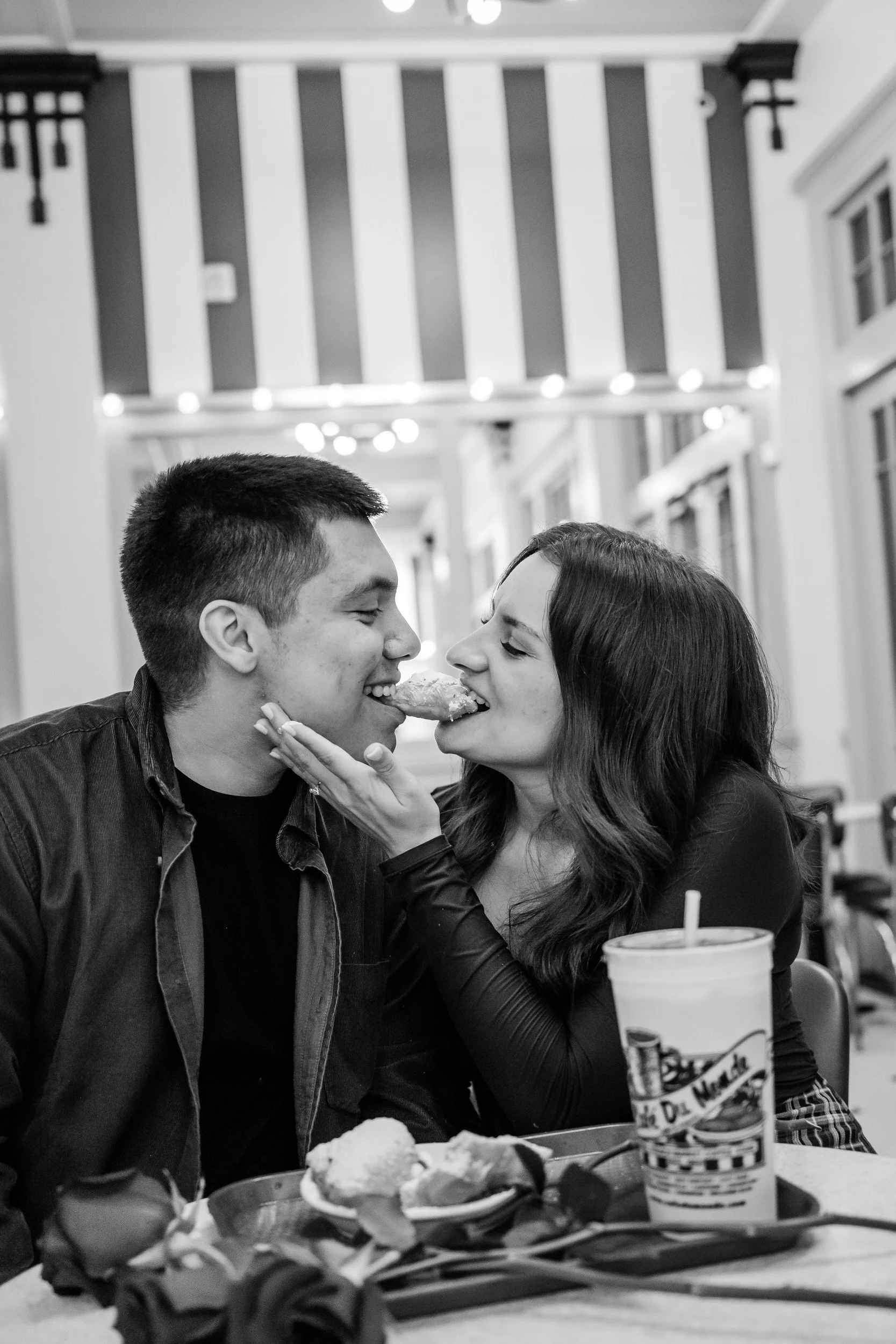 A couple each biting one side of a beignet