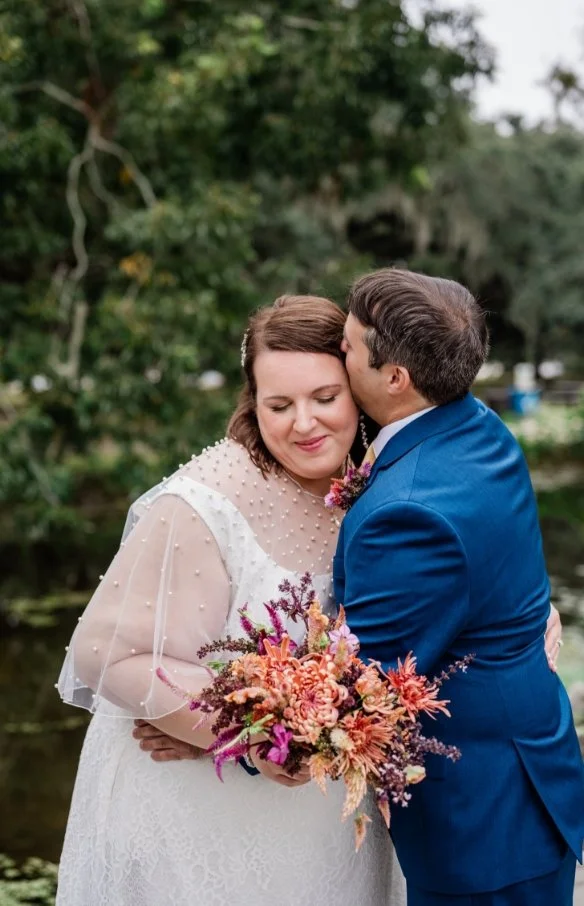 A newlywed couple hugging as one kisses the side of the other's head