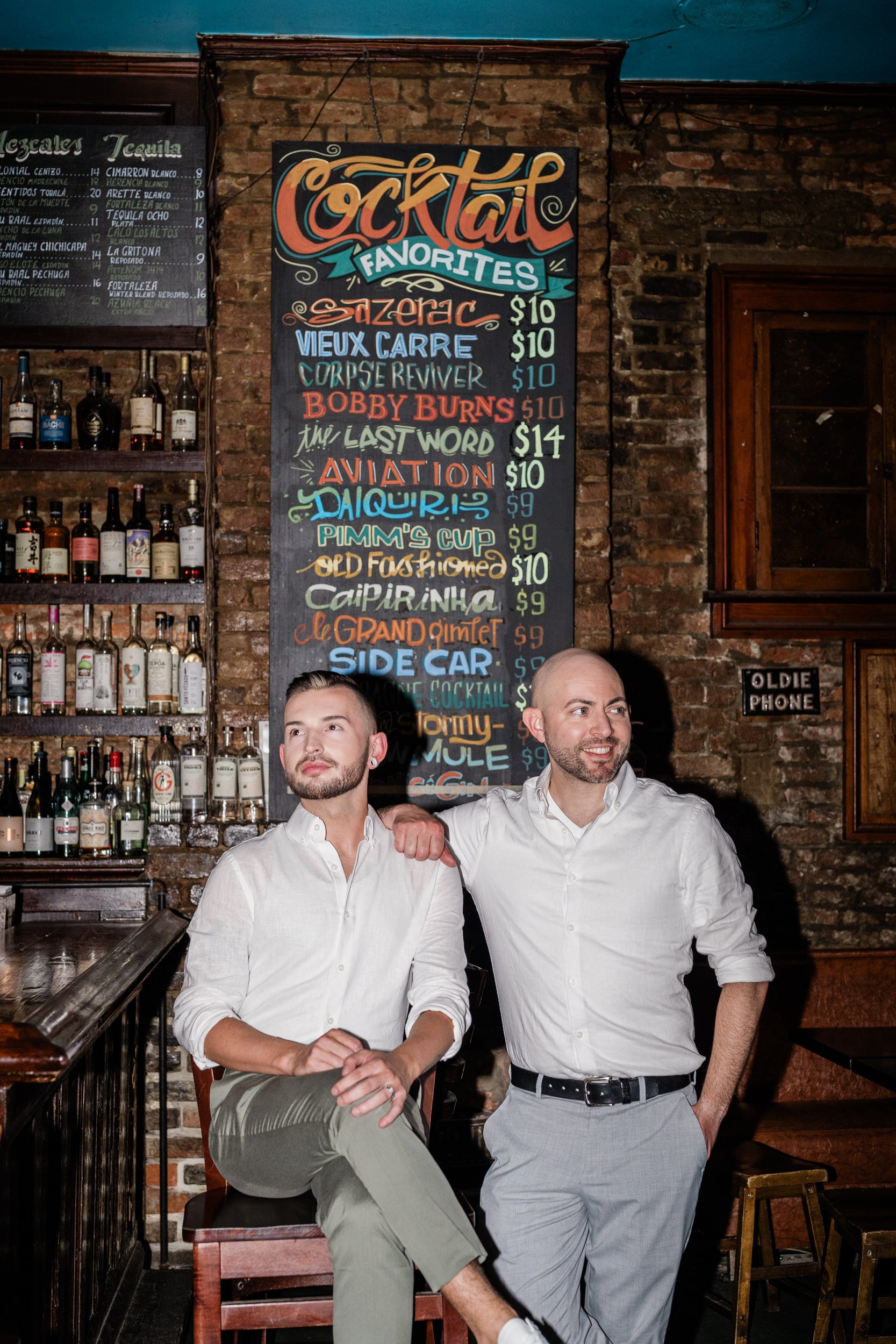 A person standing next to their partner who is sitting on a stool at a bar