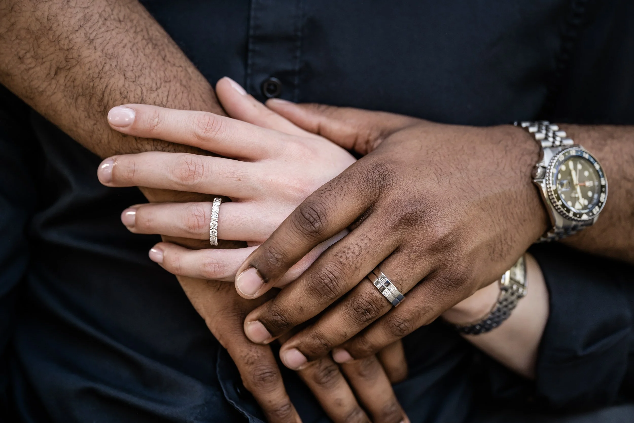 A close up of two people's hands laid on top of each other showing off engagement rings