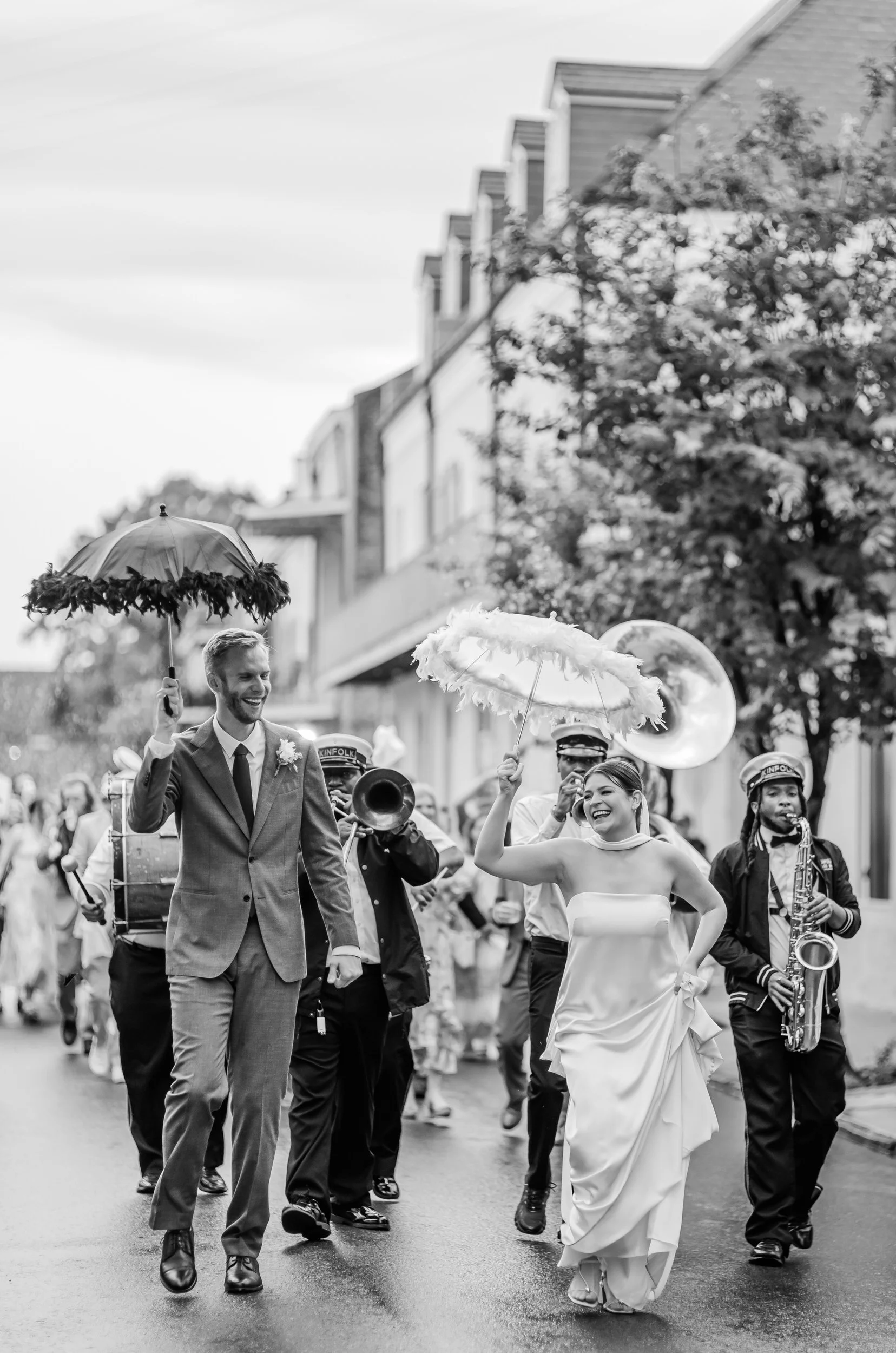 A newlywed couple walking in their second line parade after their wedding with a band behind them