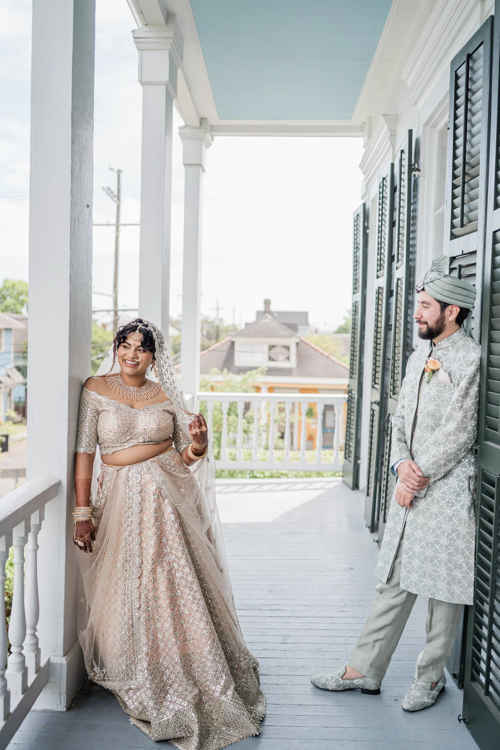 A newlywed couple standing on either side of a porch as they both smile