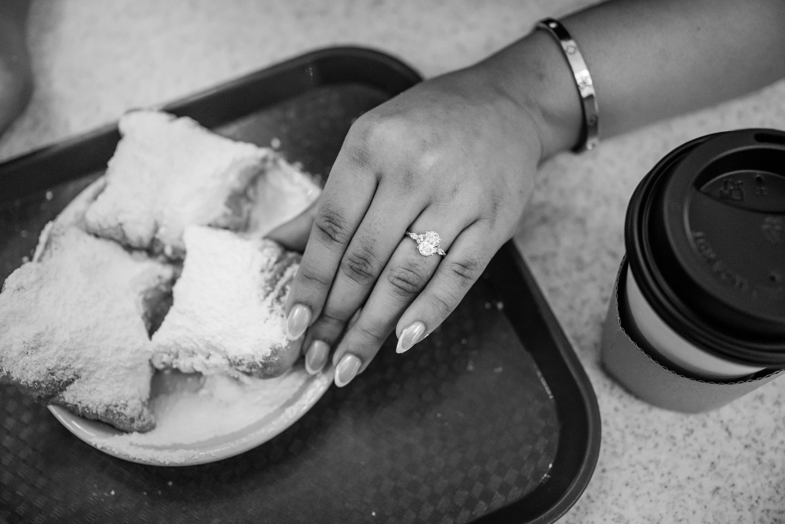 A close up of someone reaching for a beignet showing off an engagement ring
