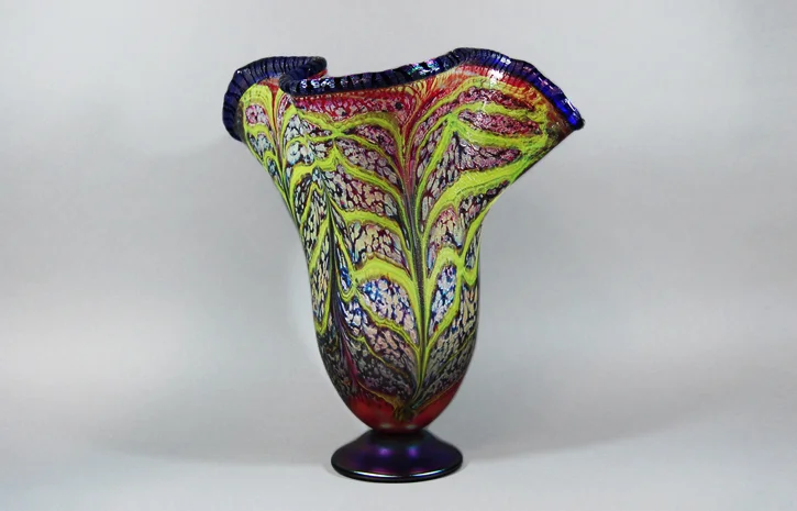 Opaque red vase with a cobalt lip and lime veining.