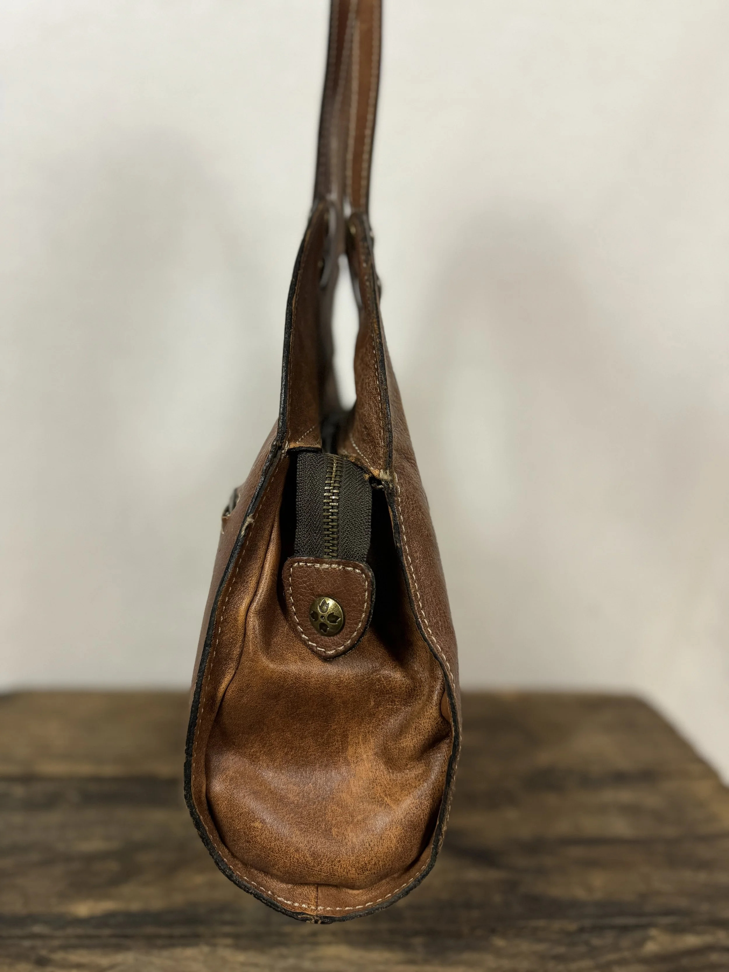 Side view of Patricia Nash Ergo leather handbag with studs in a distressed cognac-brown leather.