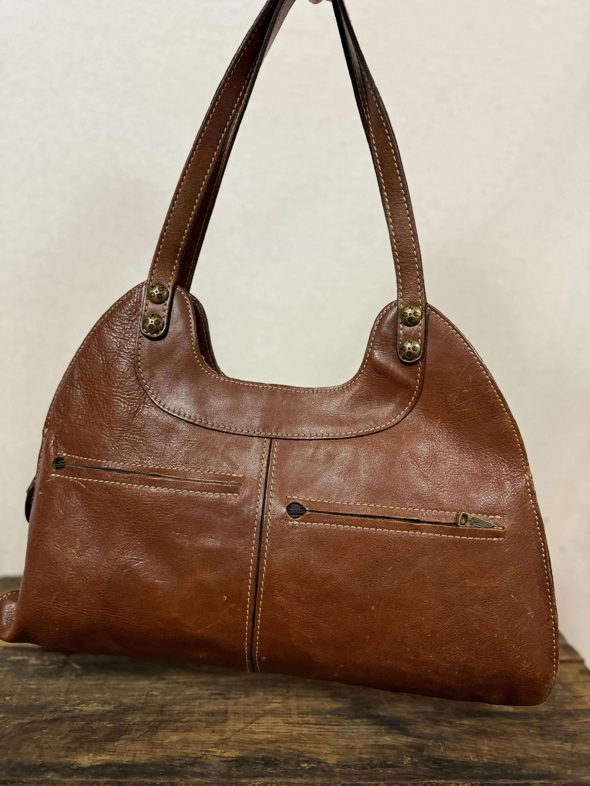 Rear view of Patricia Nash Ergo leather handbag with studs and 2 rear zipper pockets in a distressed cognac-brown leather.