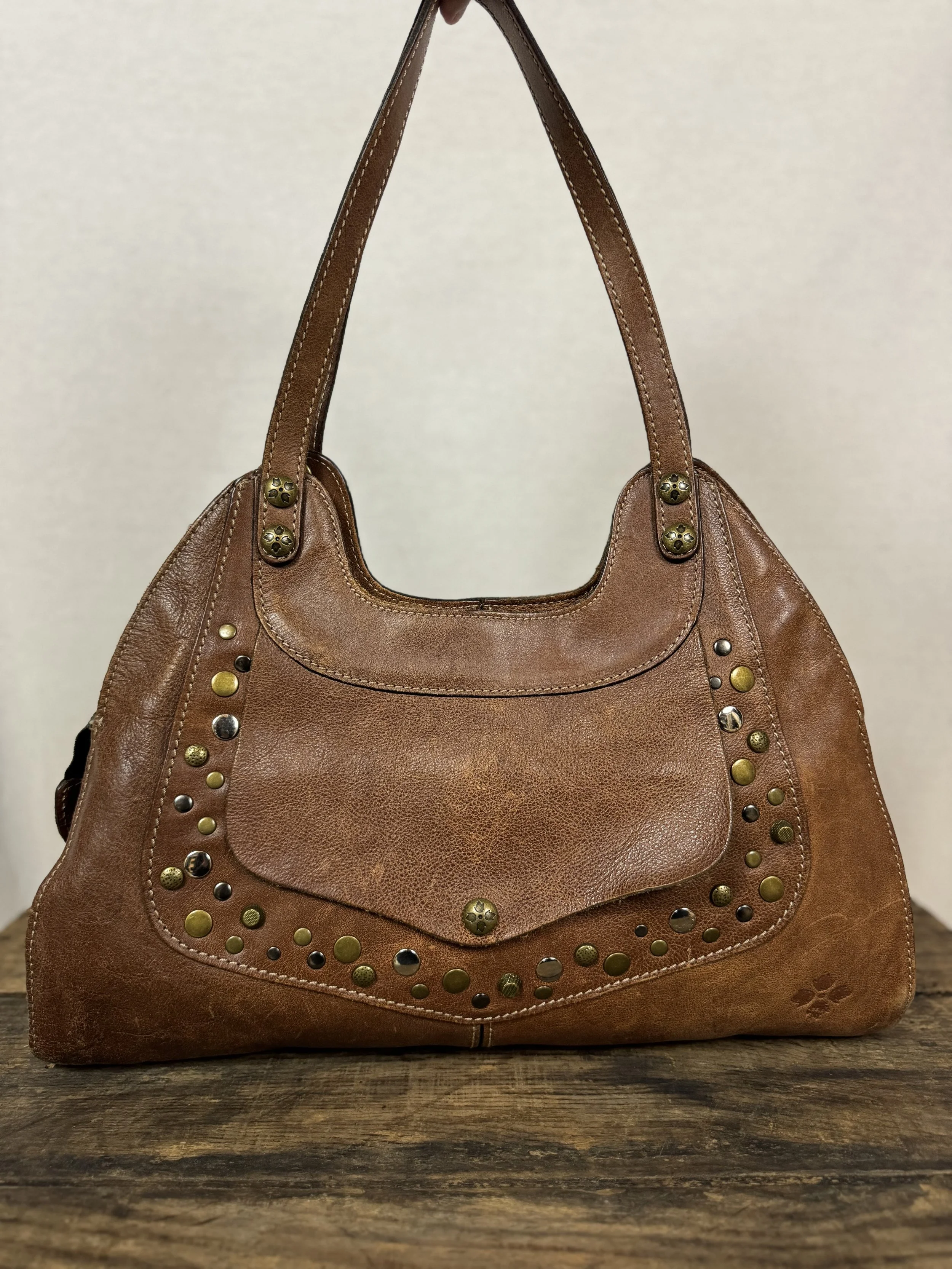 Front face of Patricia Nash Ergo leather handbag with studs and front pocket in a distressed cognac-brown leather.