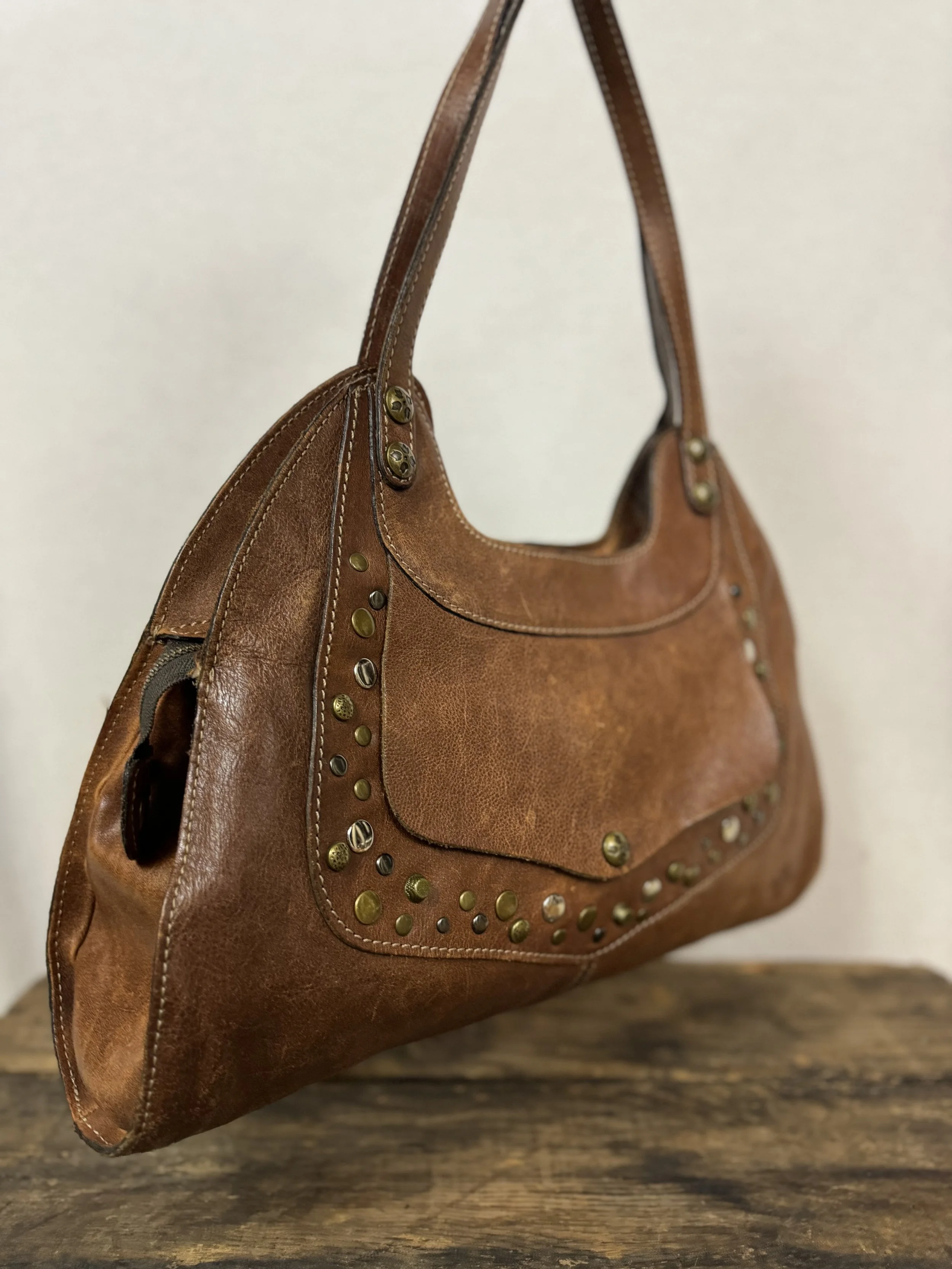 Side/Front view of Patricia Nash Ergo leather handbag with studs and front pocket in a distressed cognac-brown leather.