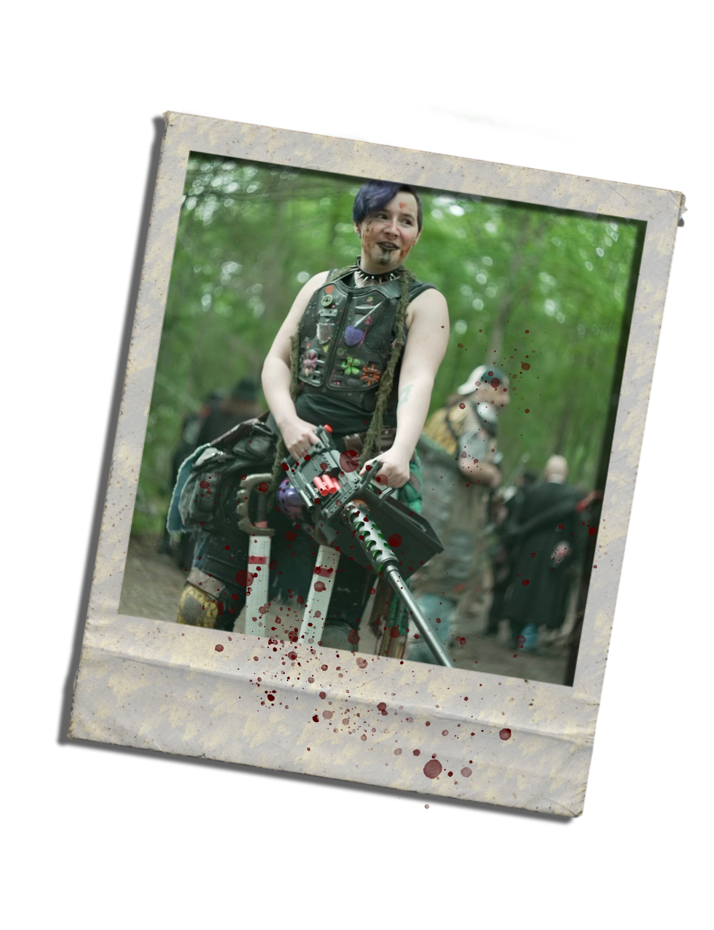 A person with dark hair, makeup, and tattoos, wearing a punk style vest, riding a motorcycle in a forest, with a second person in the background.