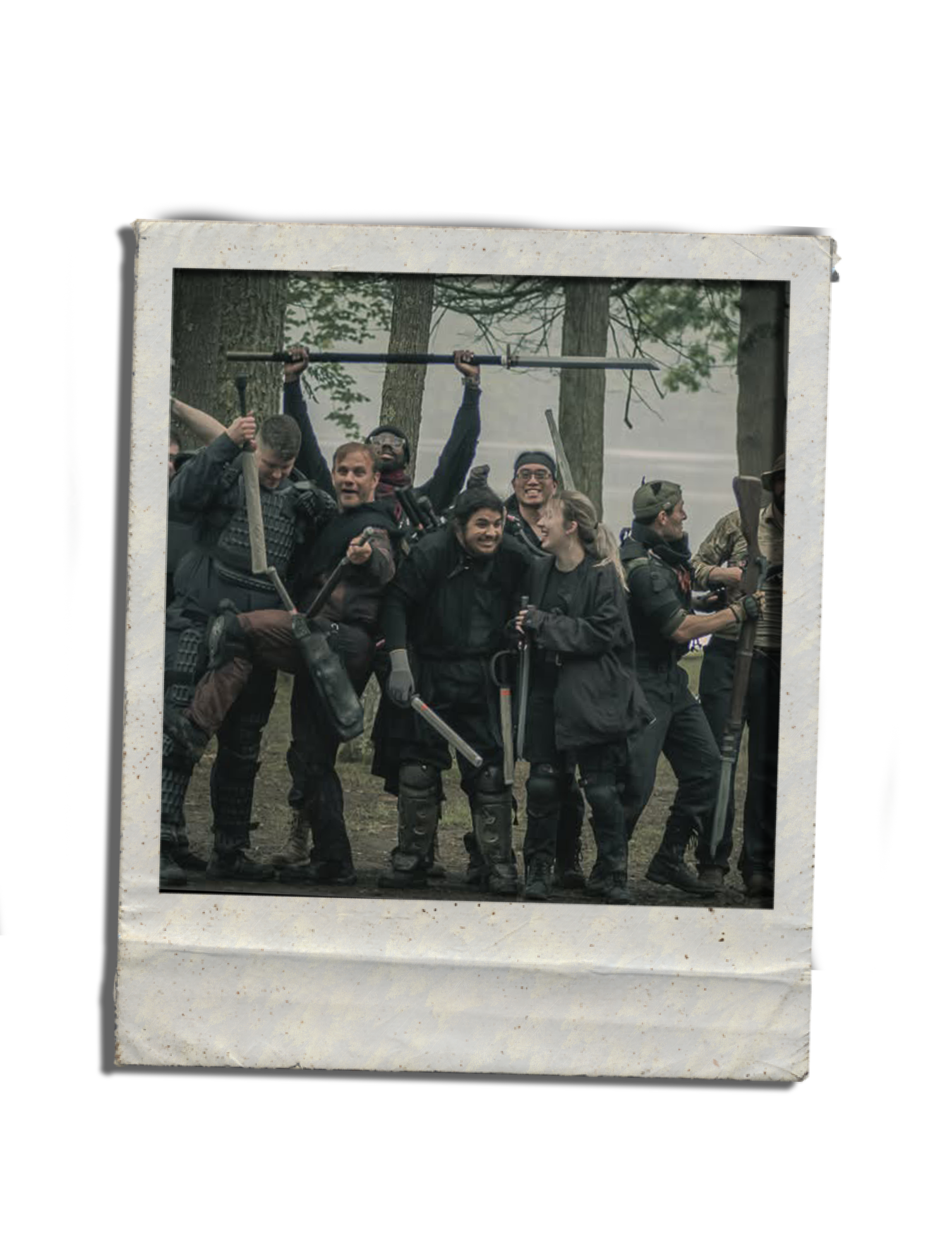 A group of people outdoors in a wooded area, smiling and holding up a framed photograph of themselves.