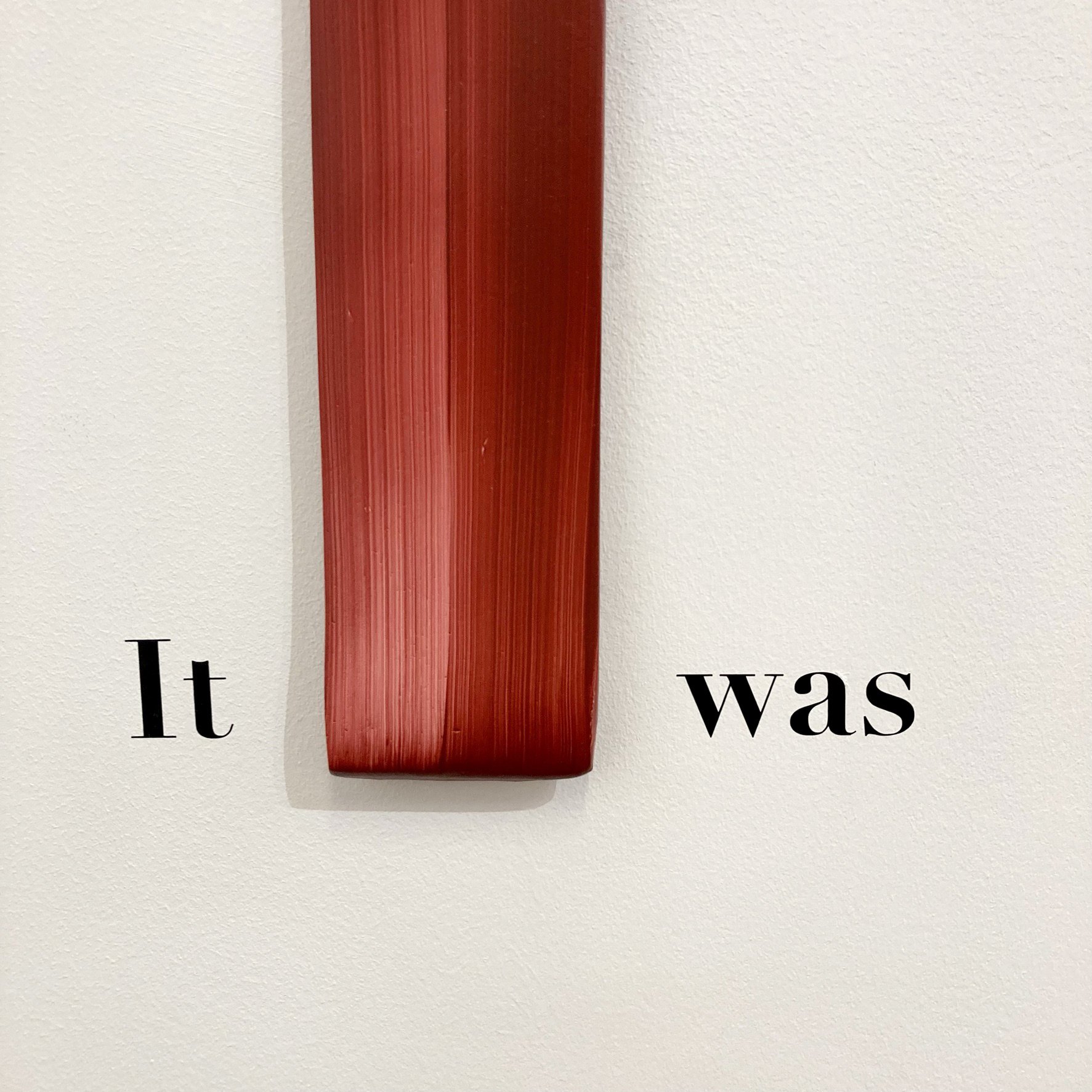 A photograph of a single painted sculptural object attached to the gallery wall, showing the detail of the brushstroke, which the artist refers to as a ‘gesture’. On either side are the words ‘it’ and ‘was’. 