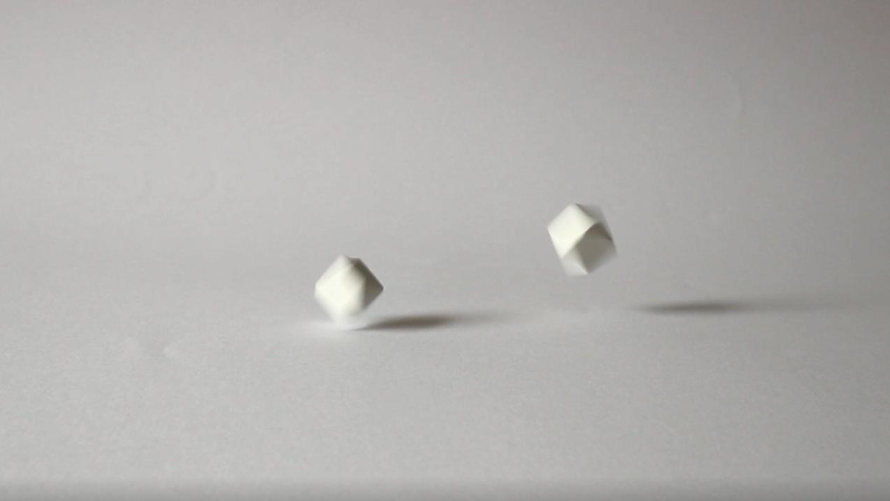  A video still of  On Some Vacant and Higher Surface  showing two dice being thrown by the artist. 