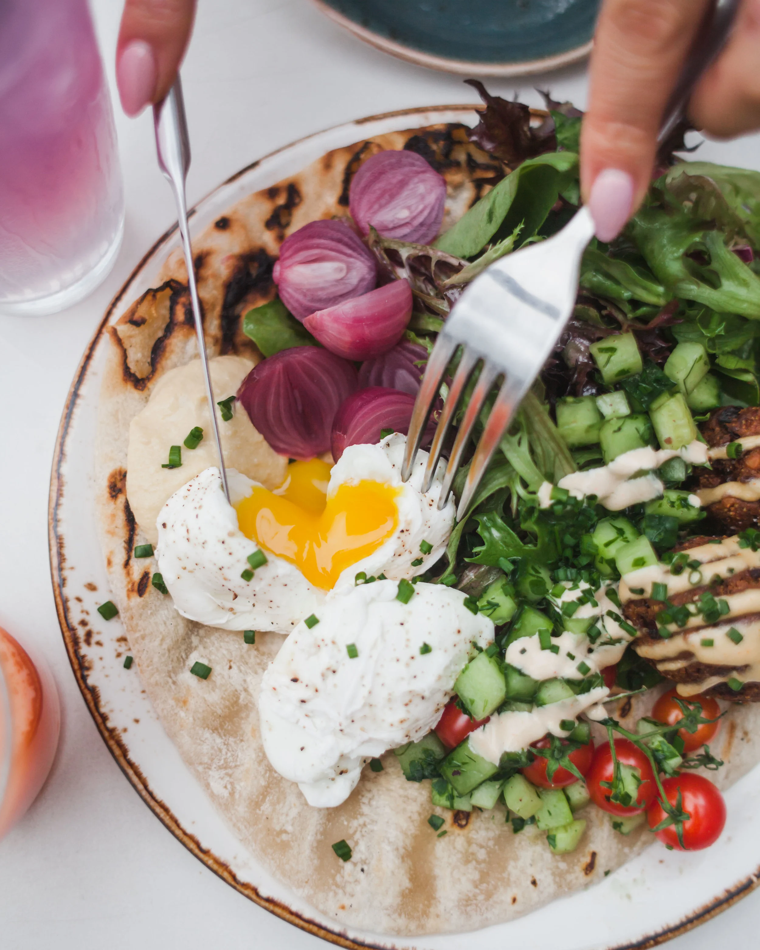 Grilled Pita with Fresh Falafel, Cucumber Salad, Tomato, Hummus, Two Poached Eggs and Lemon-Garlic Tahini