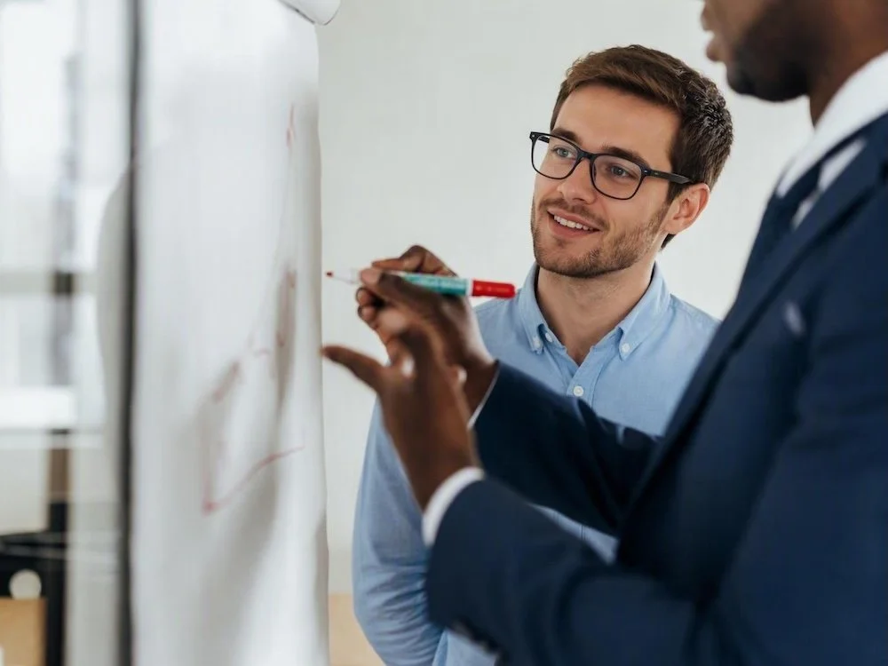 Two leaders discussing ideas at a whiteboard during a working session