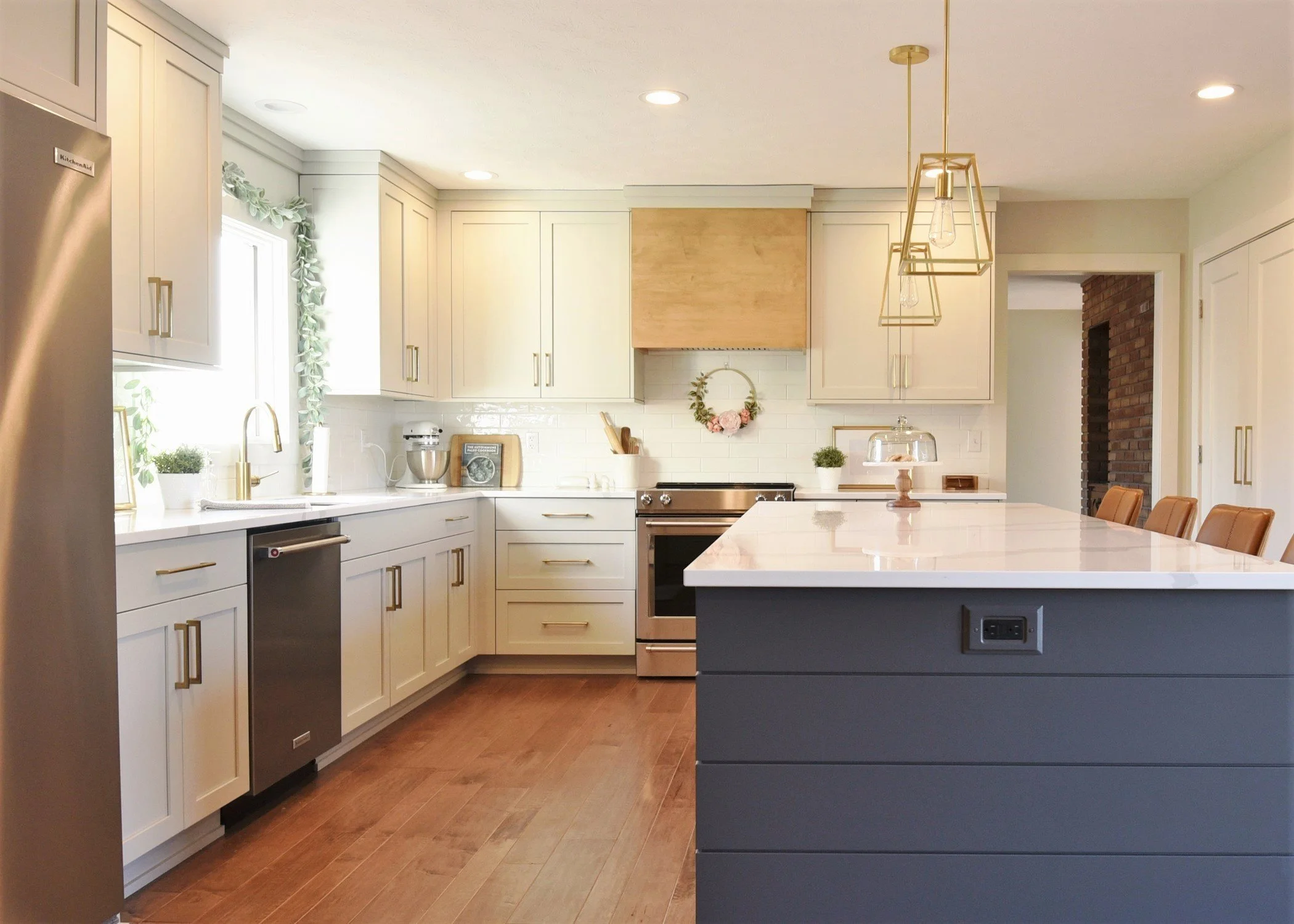 Beautiful Transitional Kitchen with Navy Shiplap Island, Cream Color Cabinets, Stained Range Hood, and Gold Hardware and Accents