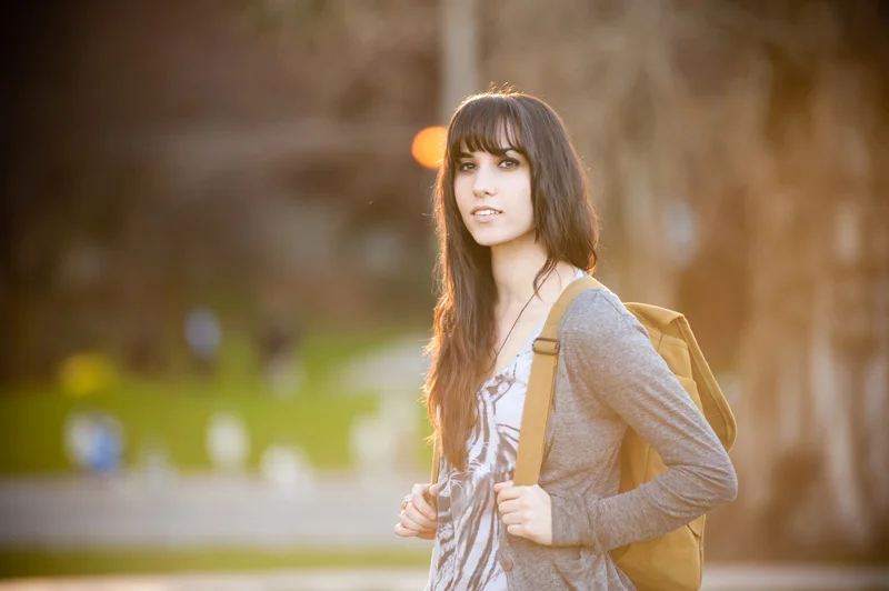 Young woman high school senior with backpack in park