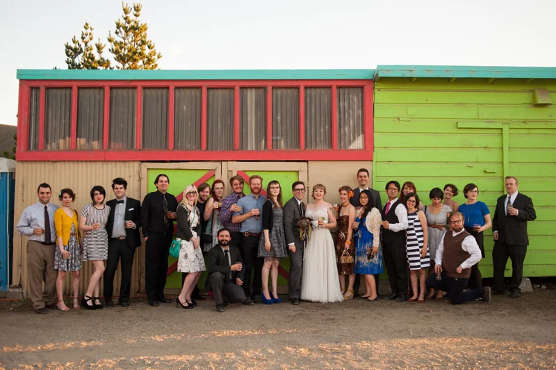 Large group portrait of wedding guests in front of colorful building